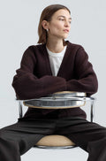 Person sitting on a modern chair wearing a dark brown wool sweater on plain background