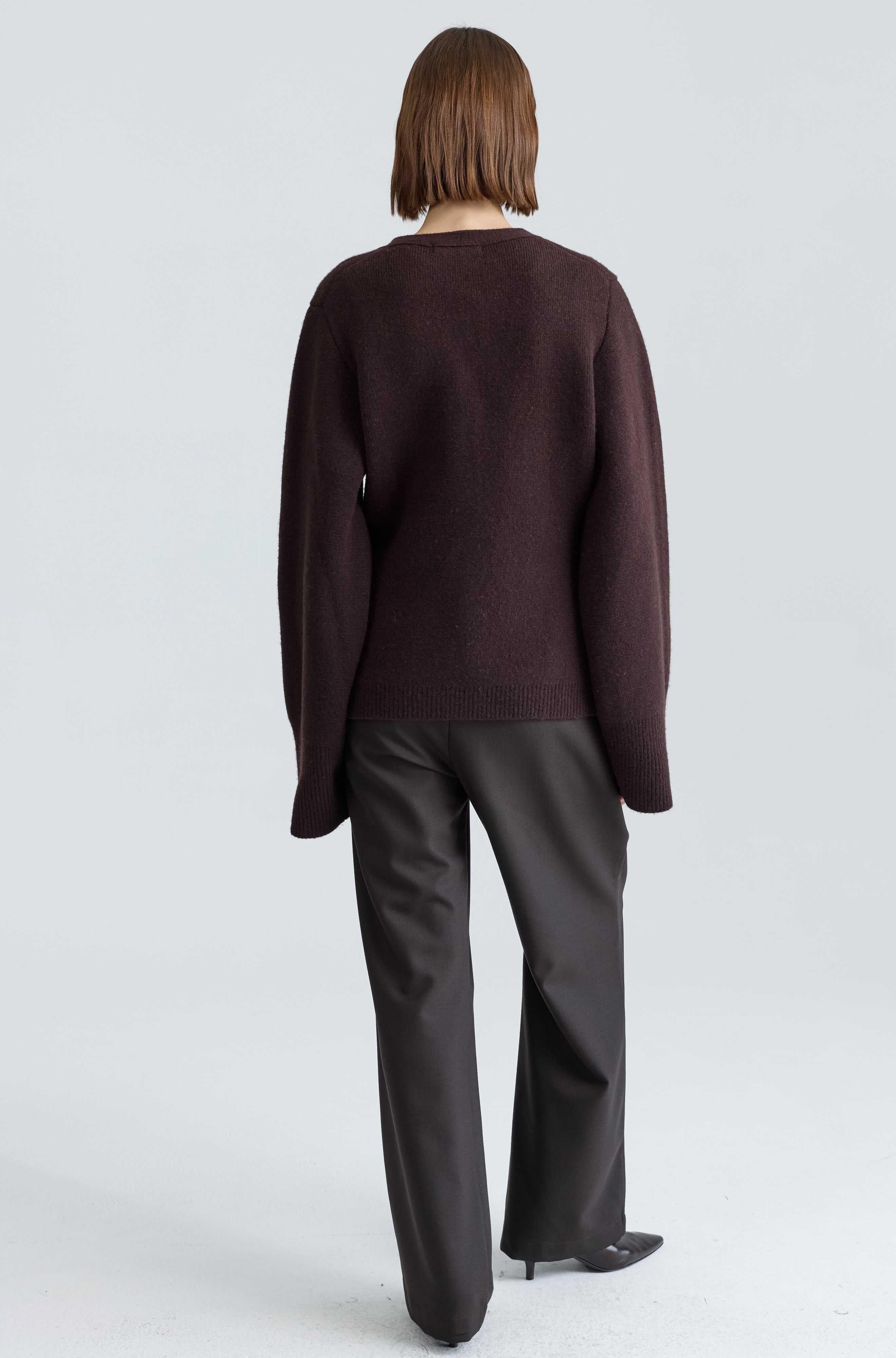 Person wearing a dark brown sweater and black pants on a light gray background