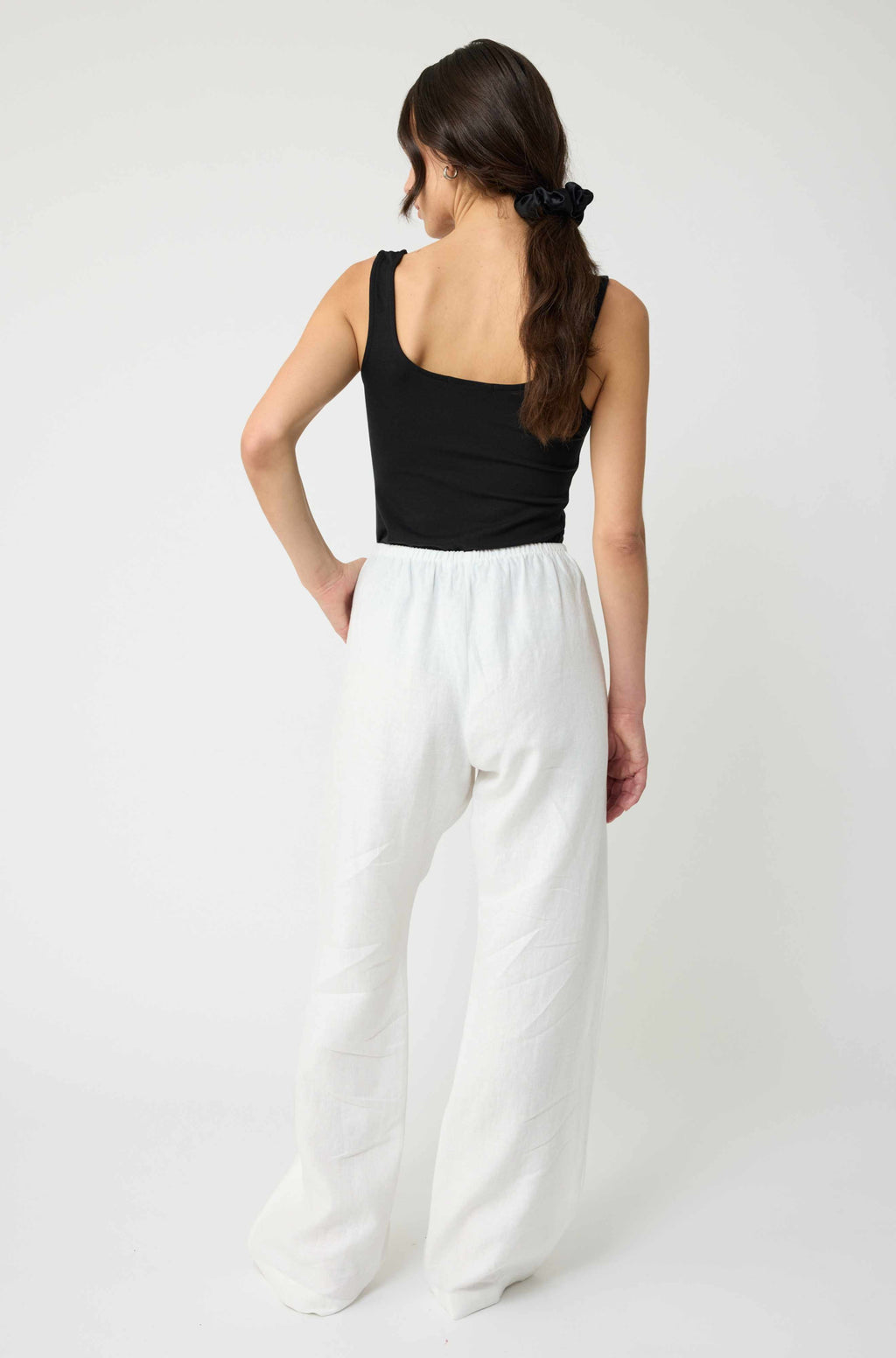 Woman wearing a black top and white pants on a white background