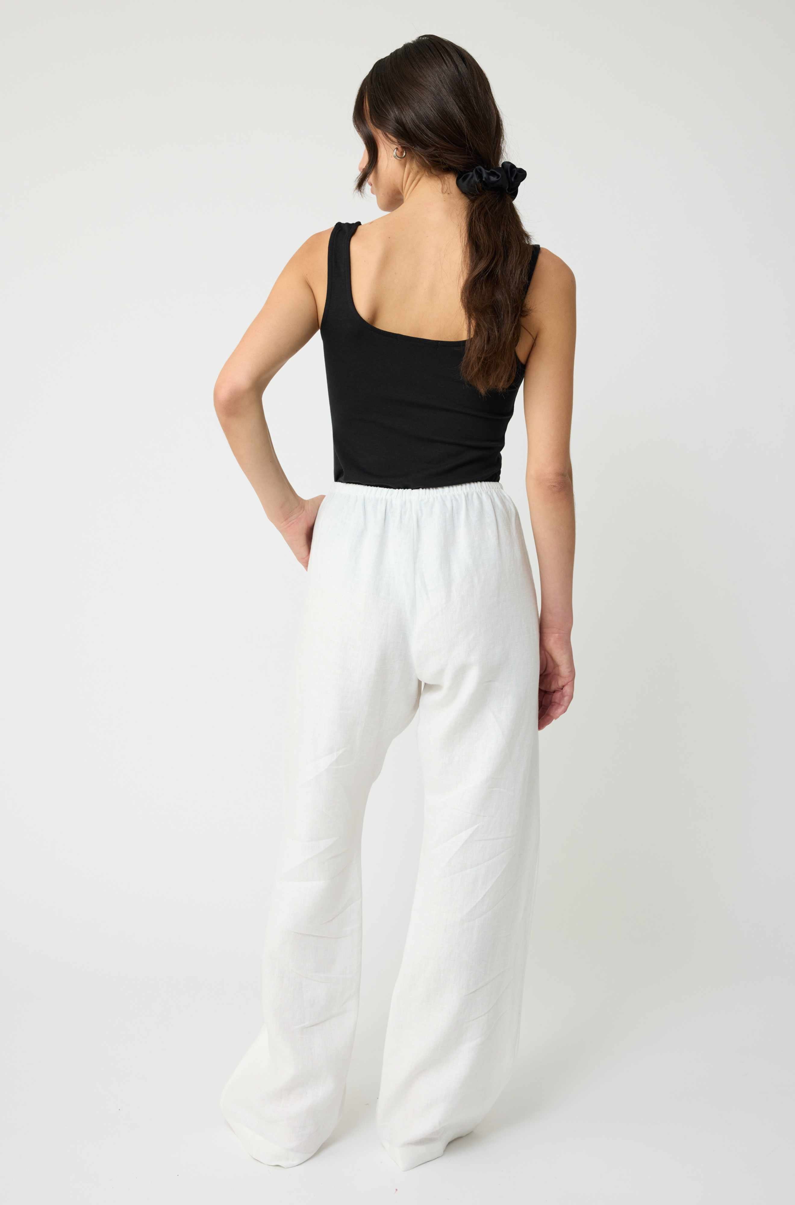 Woman wearing a black top and white pants on a white background