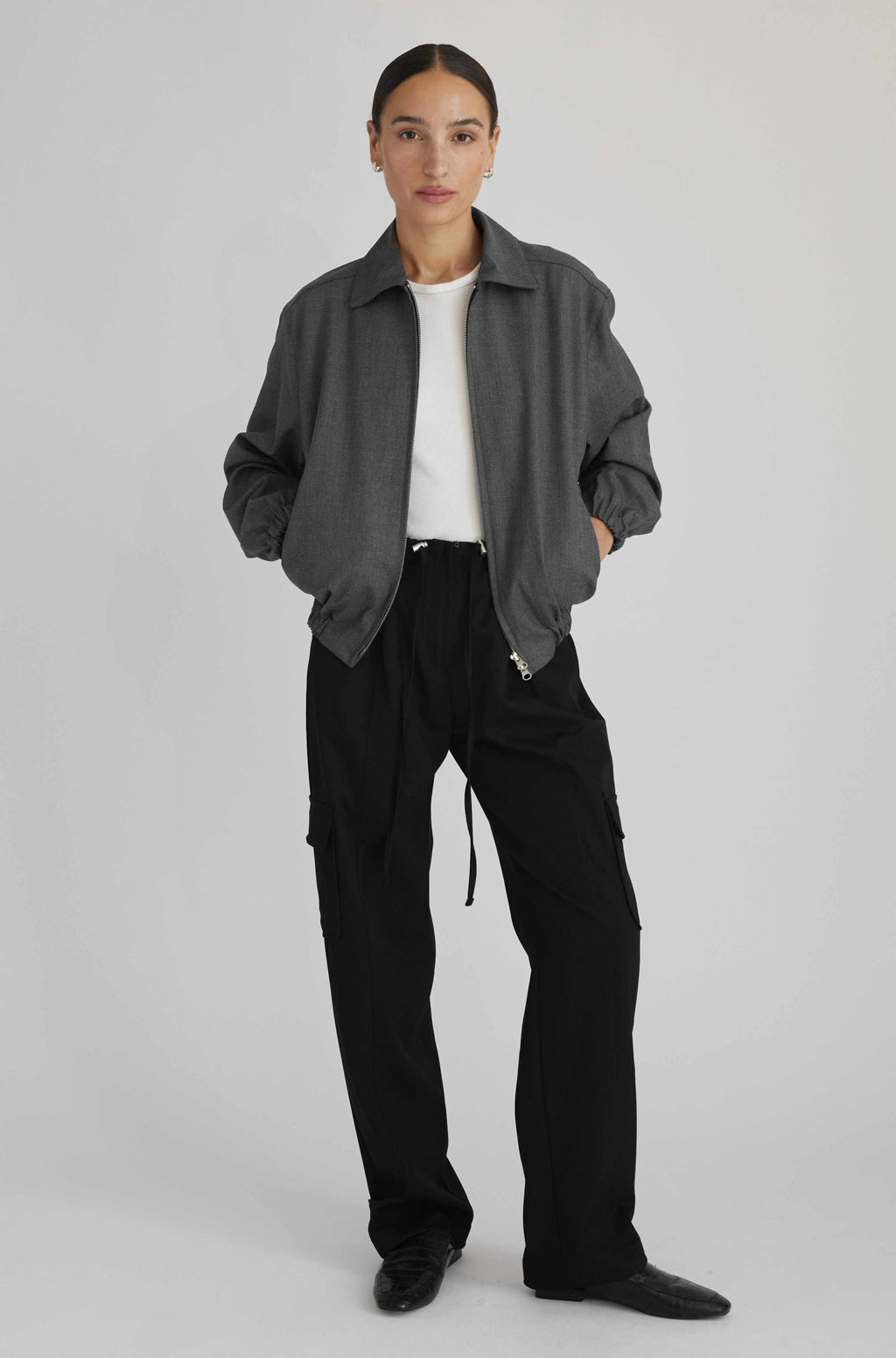 Person wearing a gray jacket and black pants on a light gray background