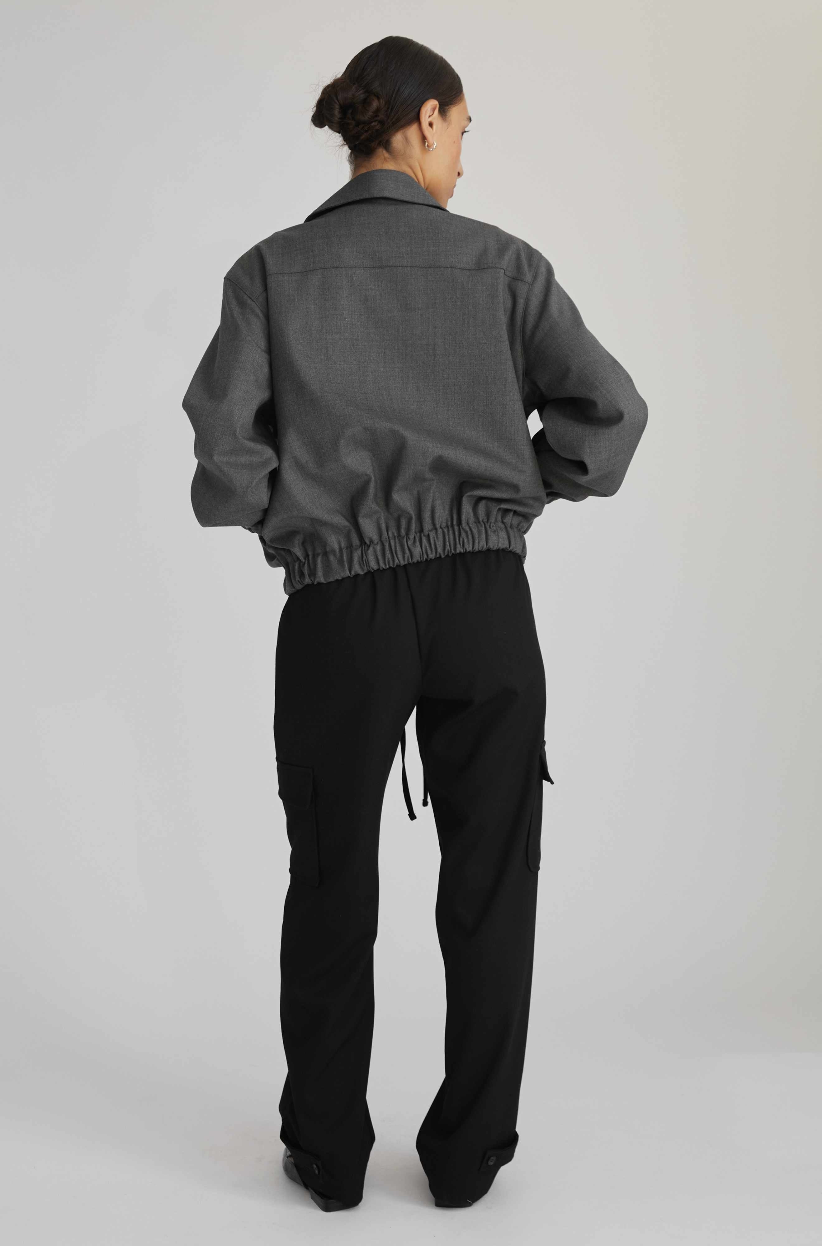 Person wearing a gray jacket and black pants on a white background