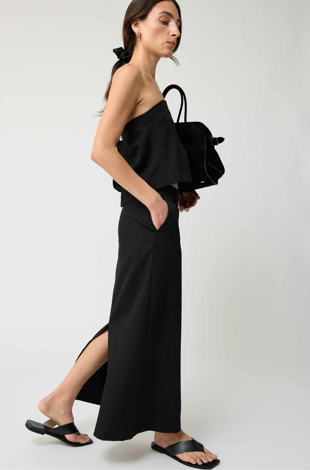 Woman wearing a black strapless top and black pants with a black handbag on a white background