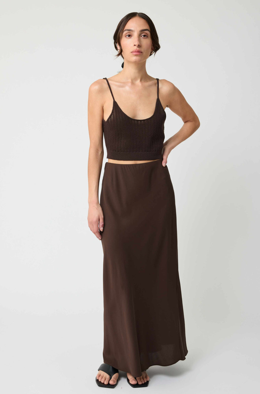 Woman wearing a brown top and long skirt on a white background