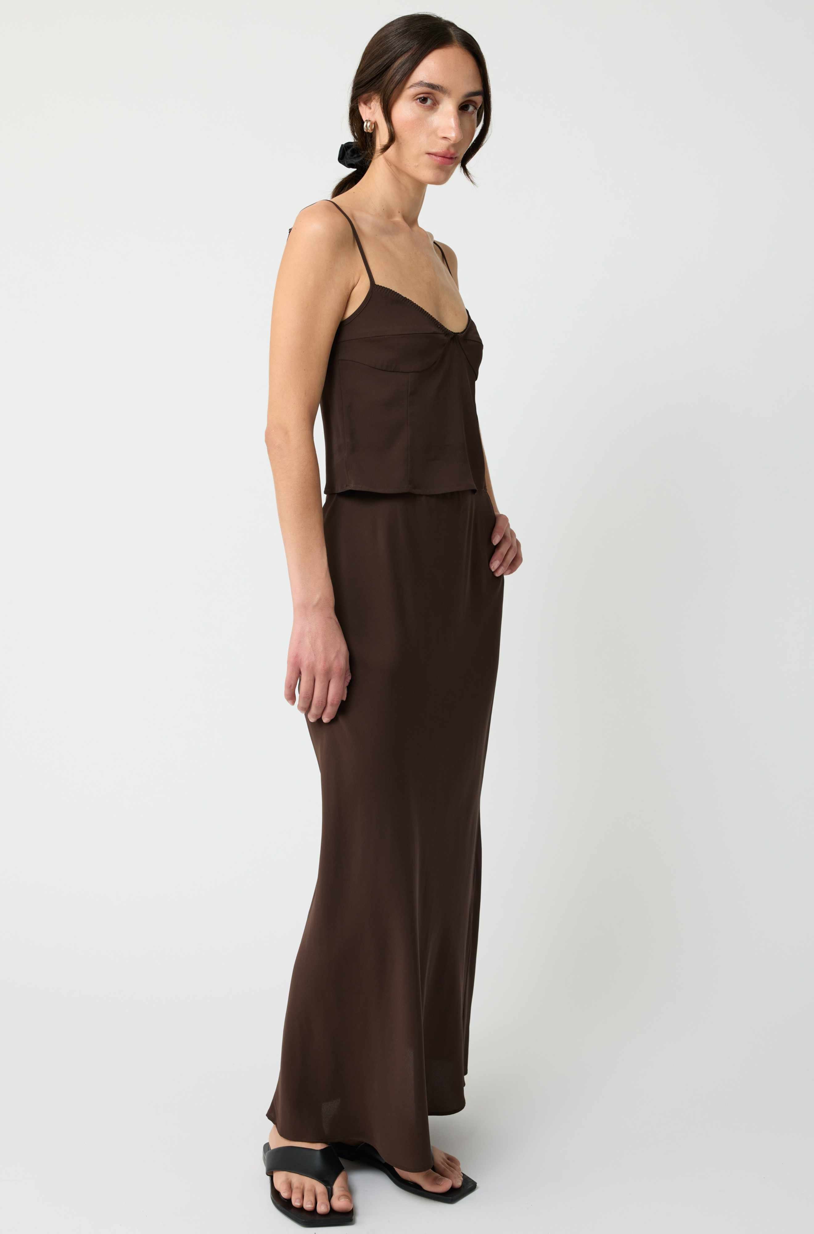 Woman wearing a brown sleeveless top and long skirt on a white background