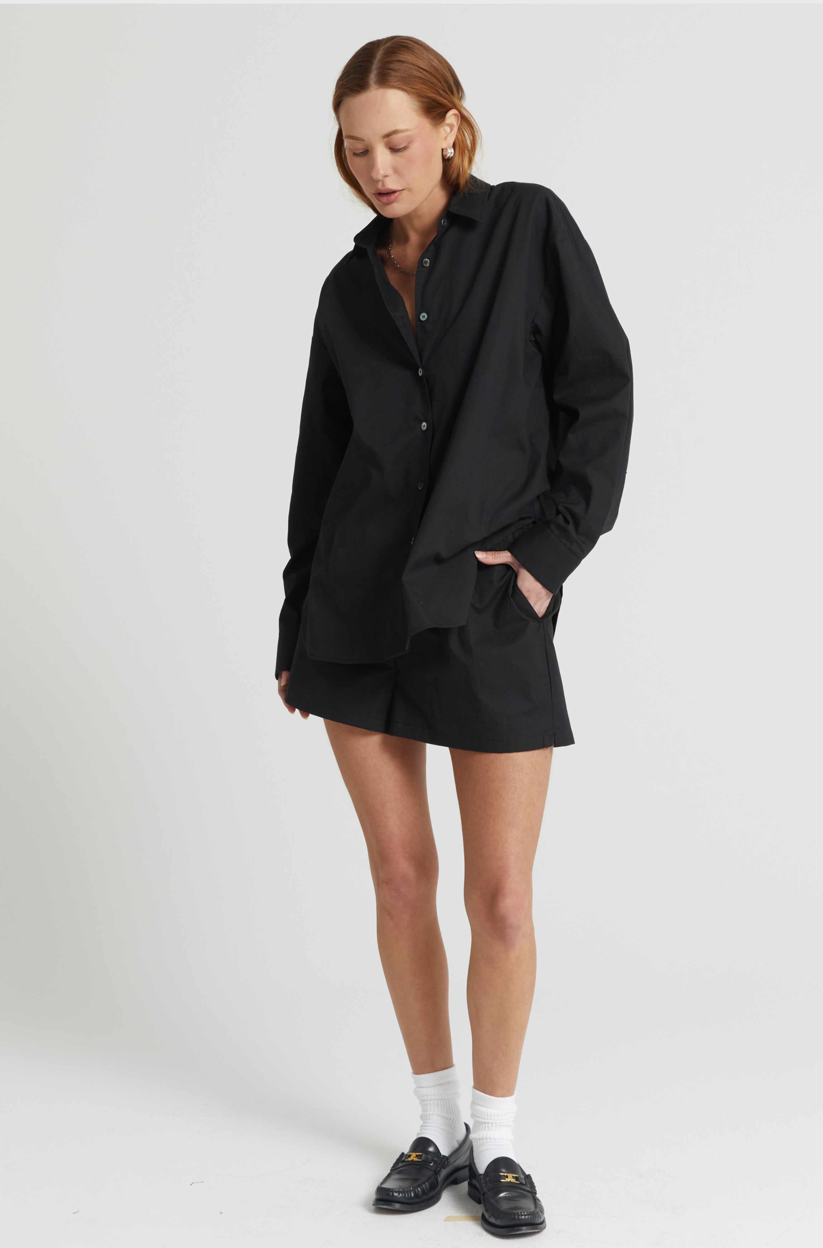 Person wearing a black oversized shirt and shorts set on a white background