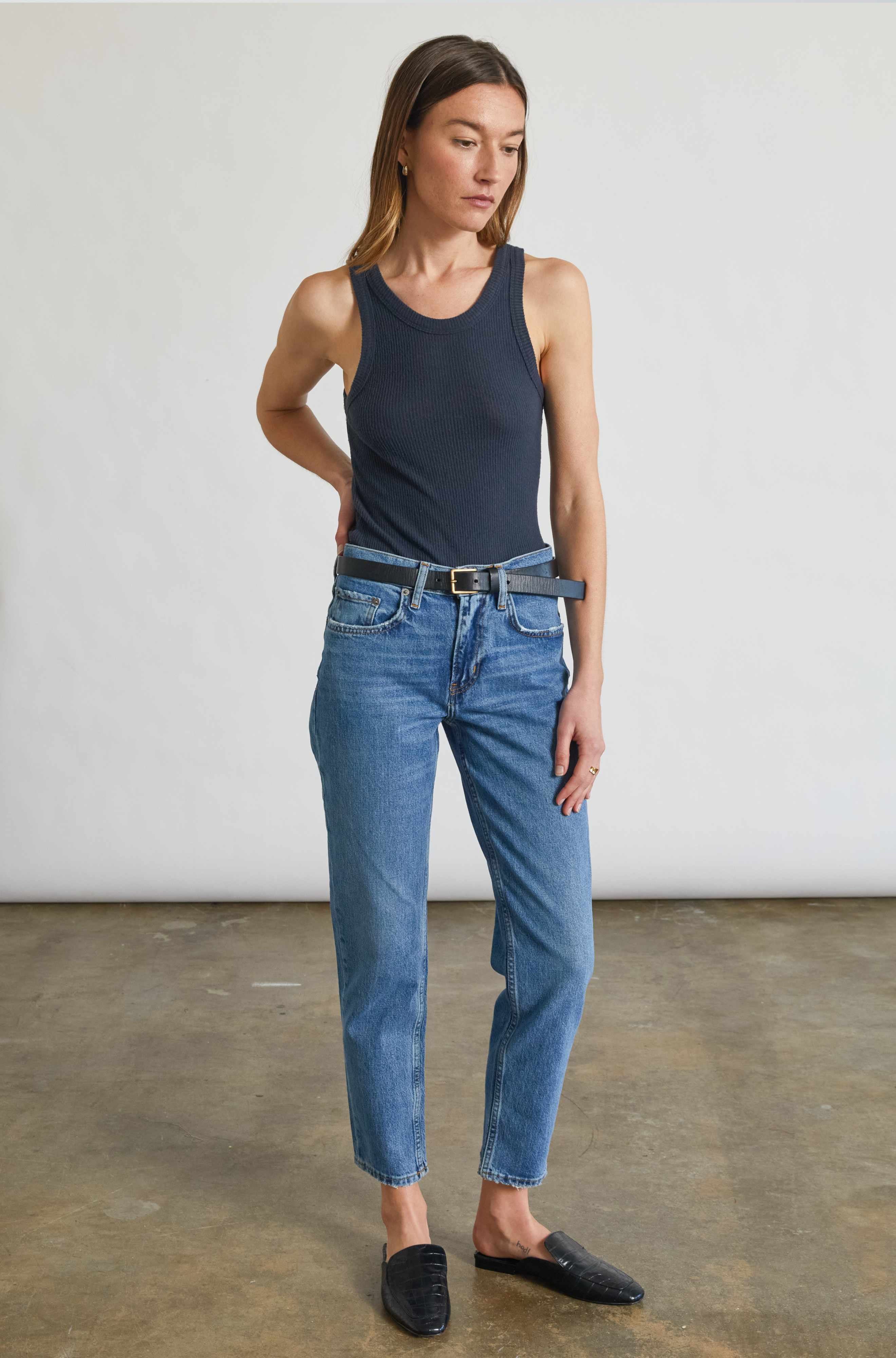 Woman wearing a navy tank top and blue jeans standing against a plain background