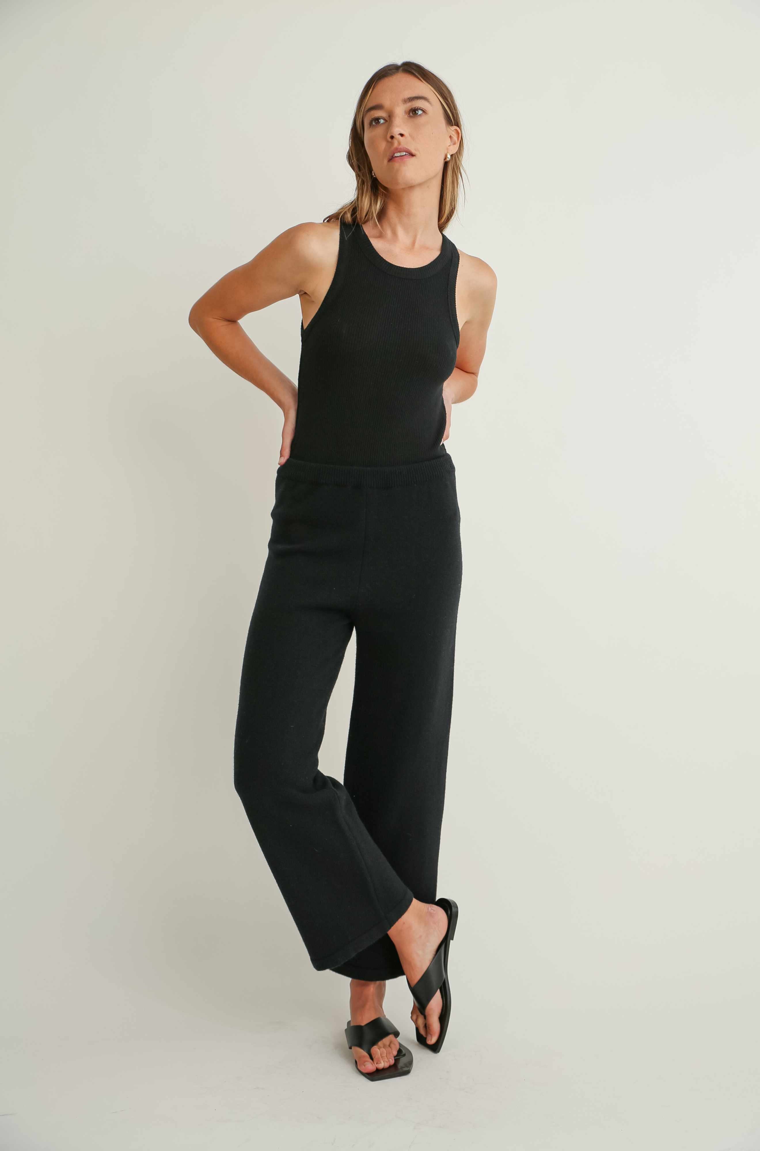 Woman wearing a black sleeveless top and pants on a light background