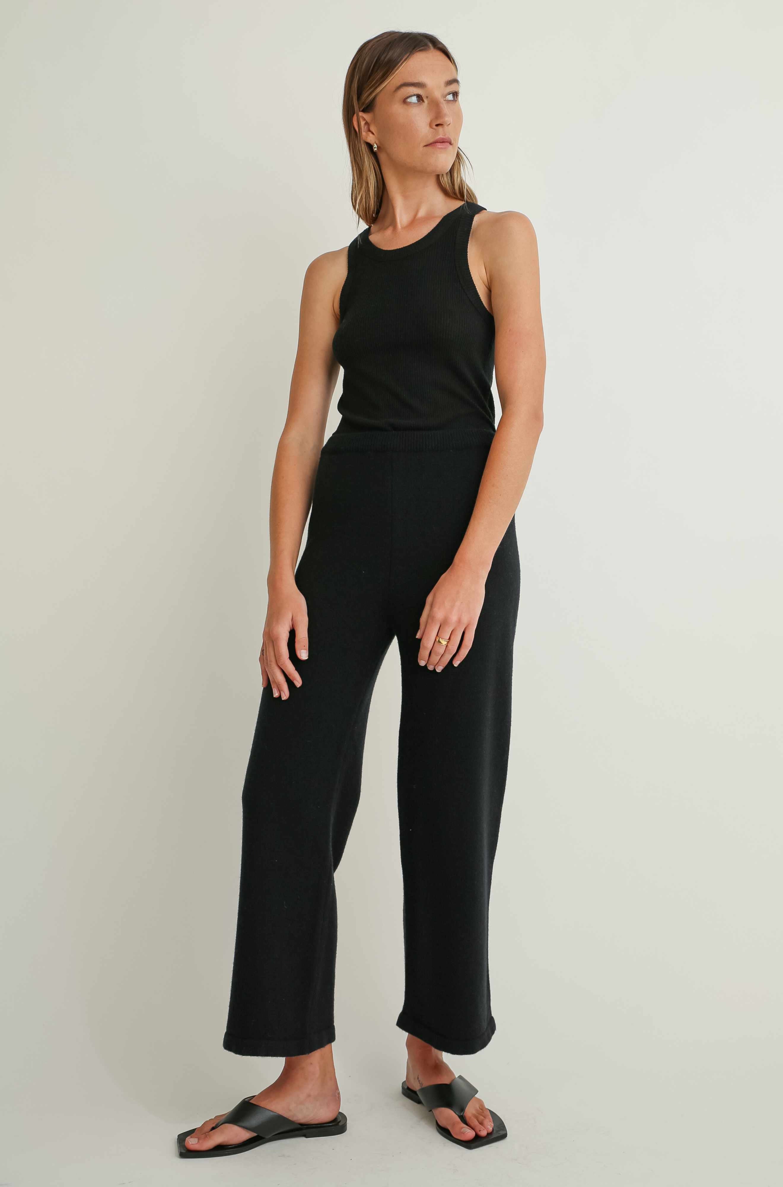 Woman wearing a black sleeveless top and pants on a light background