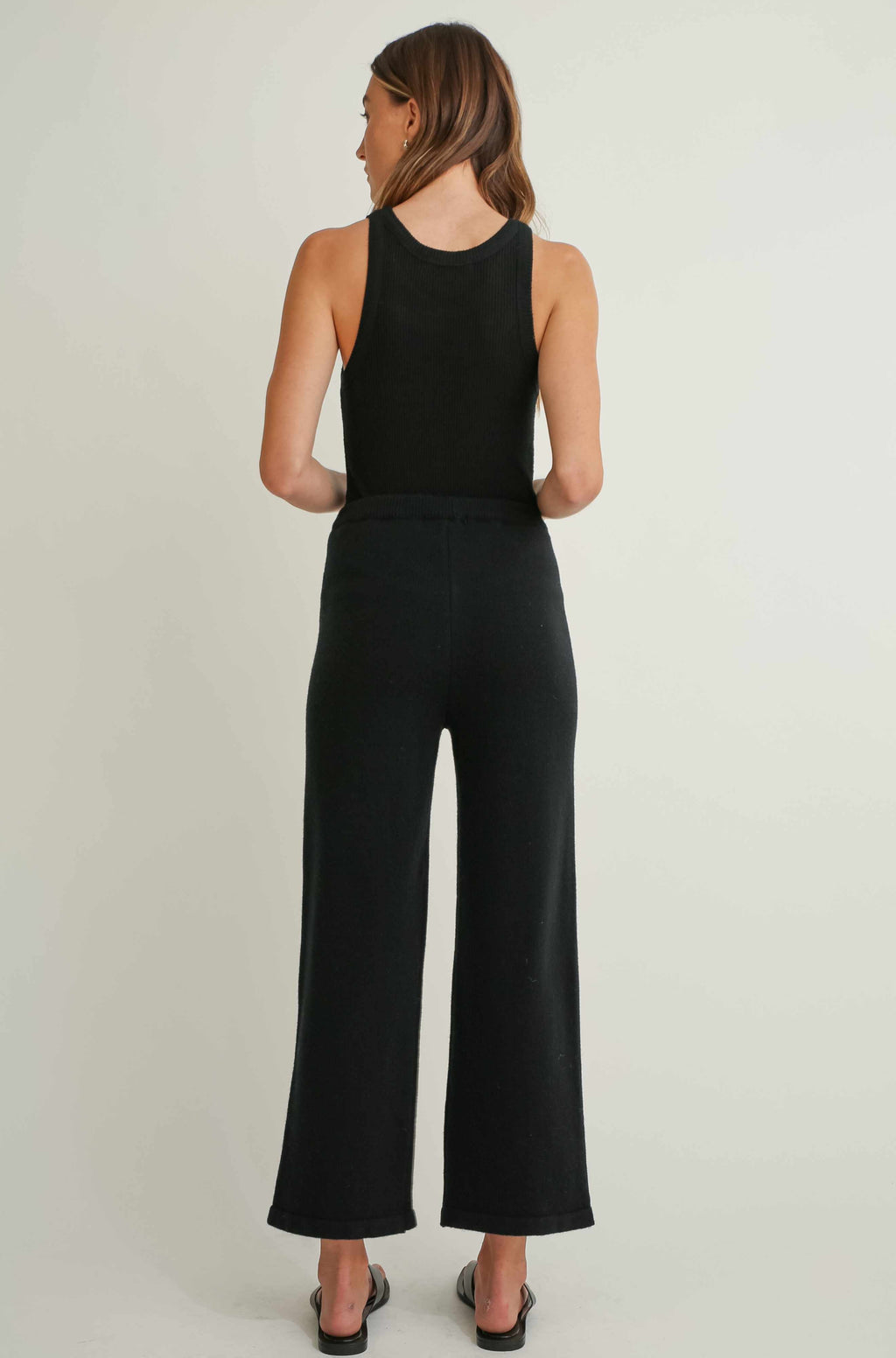 Woman wearing a black sleeveless top and wide-leg pants on a plain background