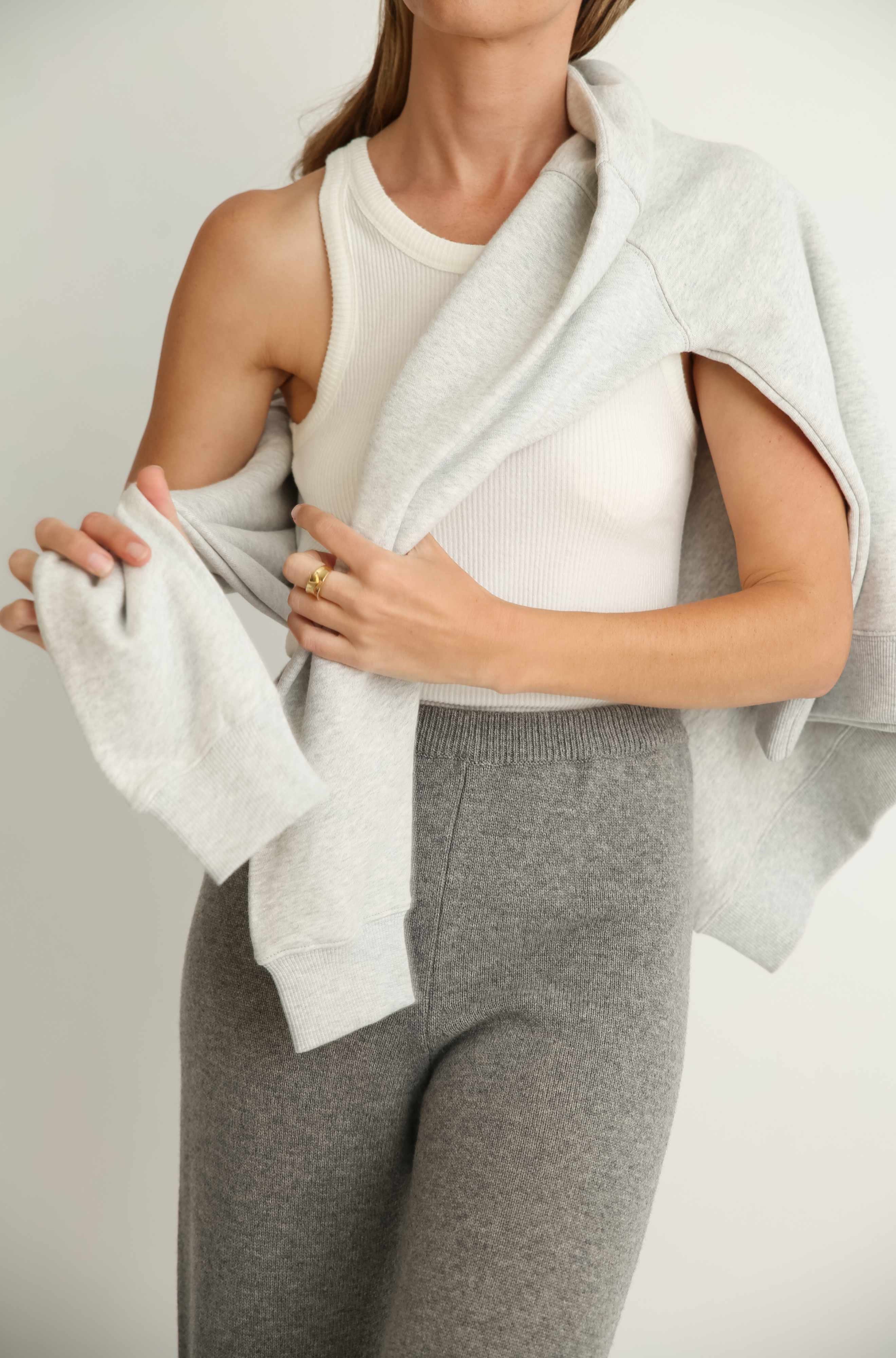 Person wearing a white tank top and gray pants with a light gray wrap around their shoulders against a plain background.