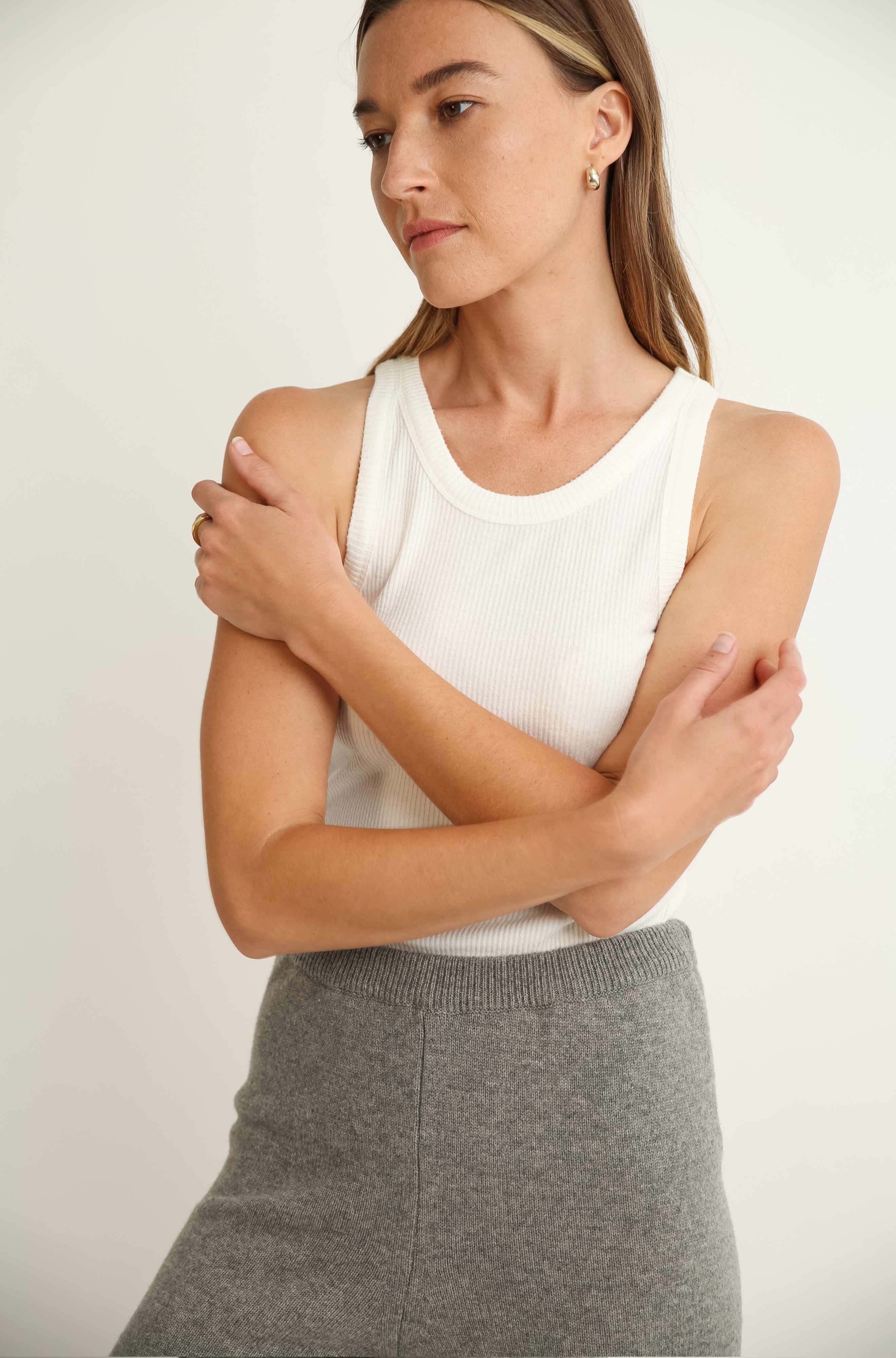 Woman wearing a white sleeveless top and gray skirt against a plain background