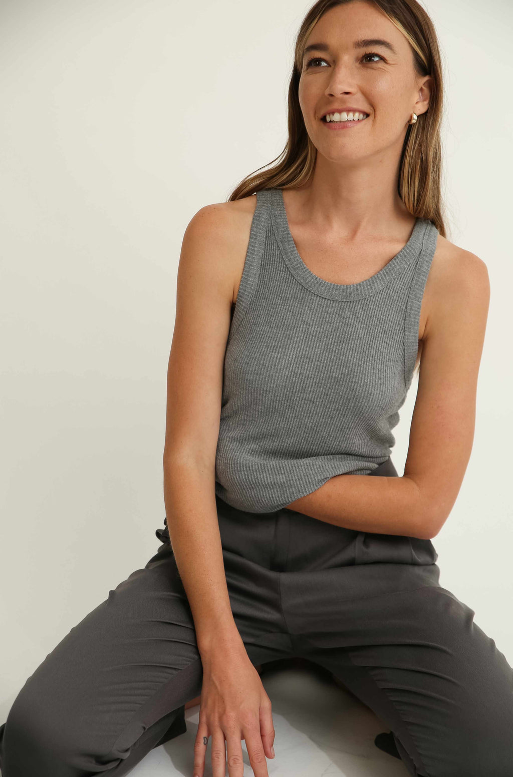 Woman wearing a gray sleeveless top and pants sitting on a white surface.