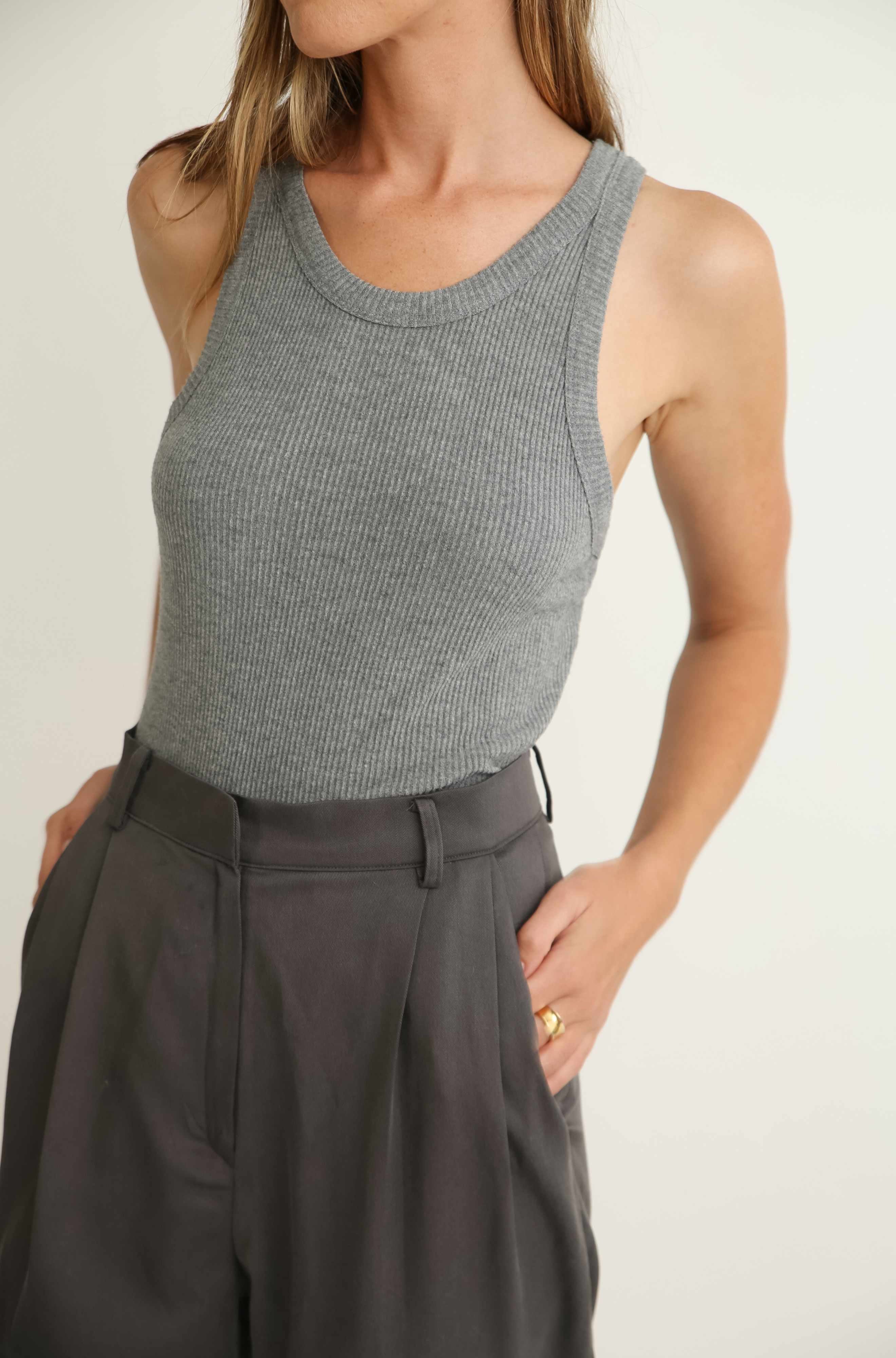 Person wearing a gray sleeveless top and dark pants on a plain background