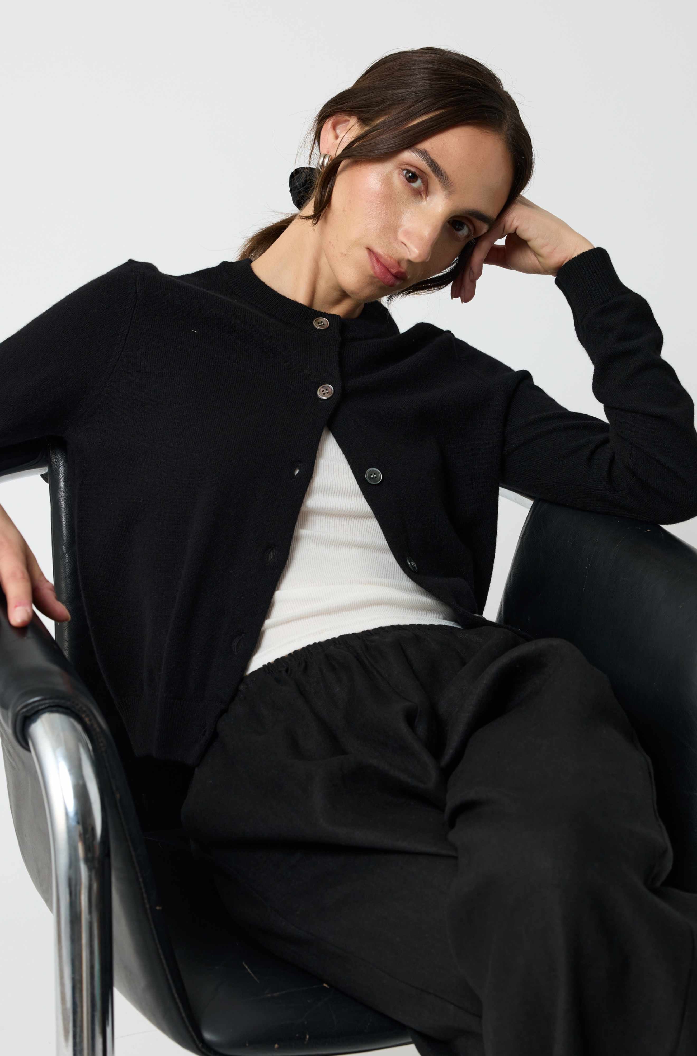 Woman sitting in a chair wearing a black cardigan over a white shirt.
