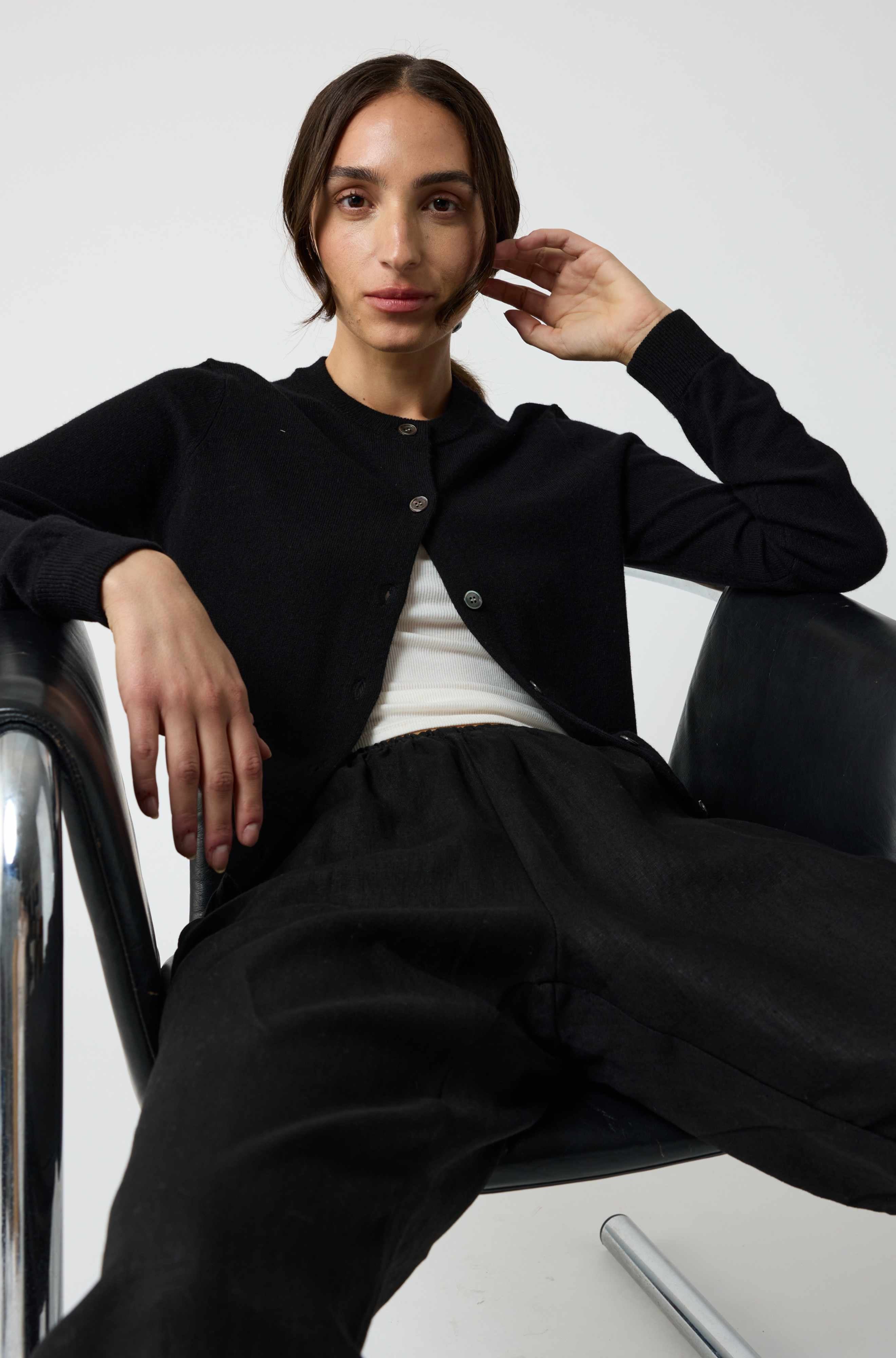 Person wearing a black jacket and pants sitting on a chair against a white background