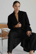 Person wearing a black outfit sitting on a chair with a plain background