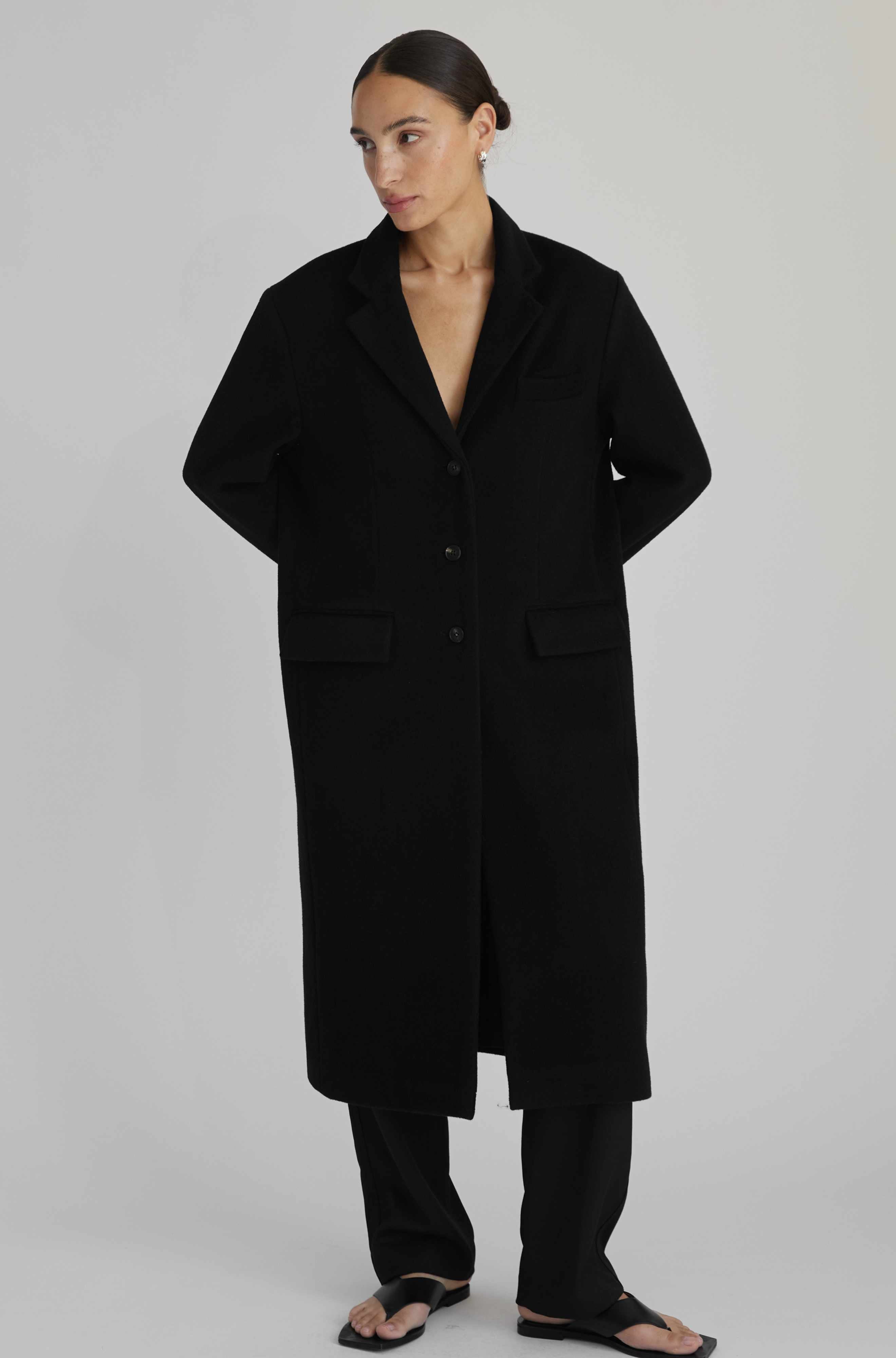 Person wearing a long black coat on a plain background