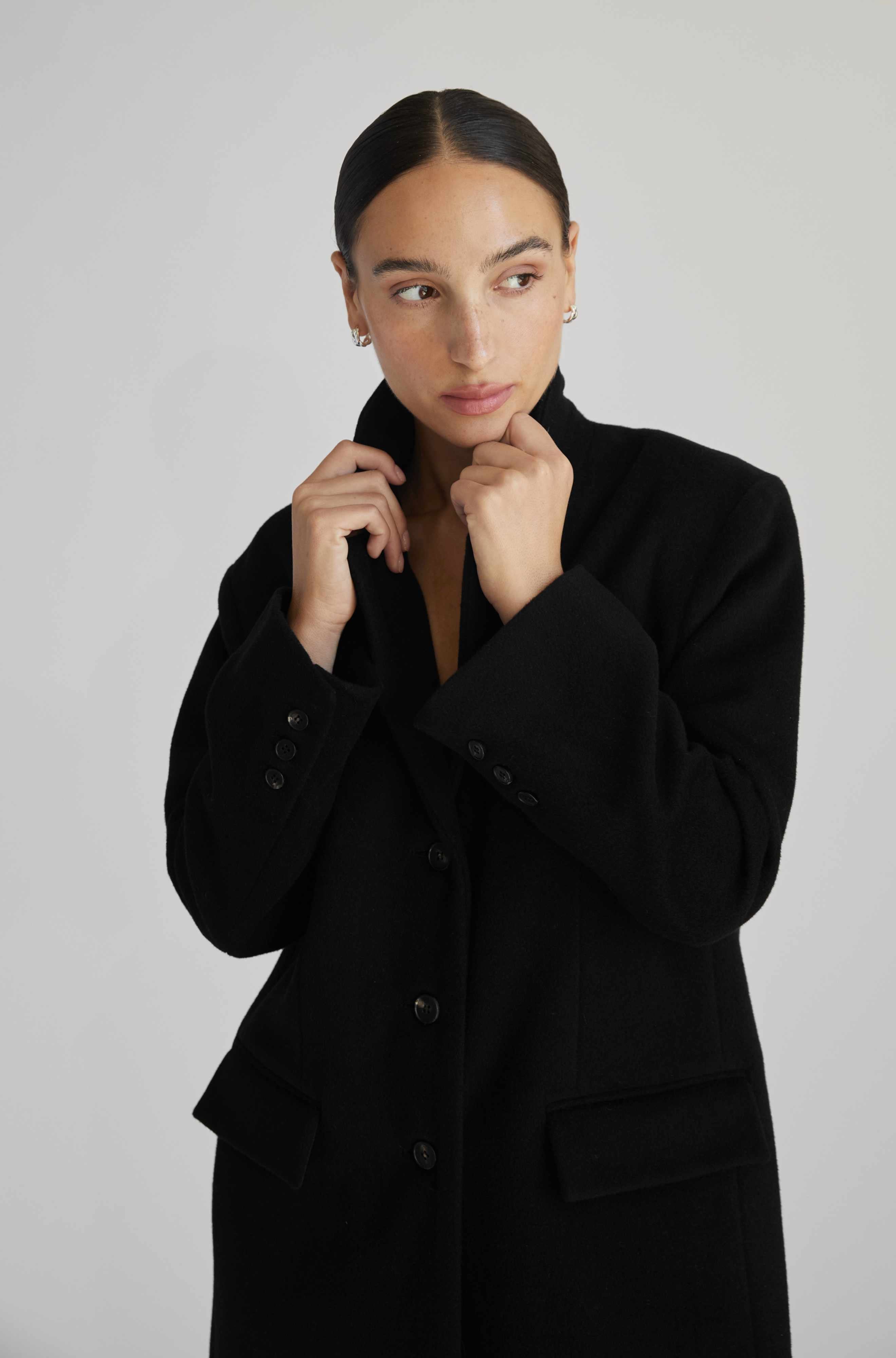 Woman wearing a black coat against a plain background