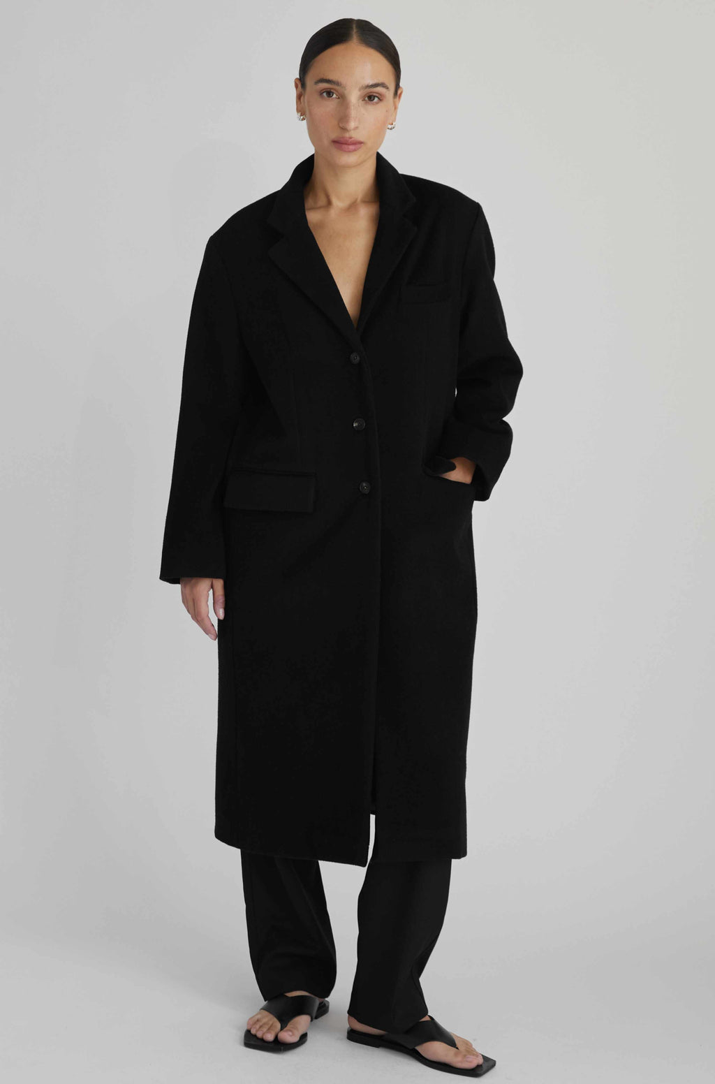 Person wearing a black coat on a plain background