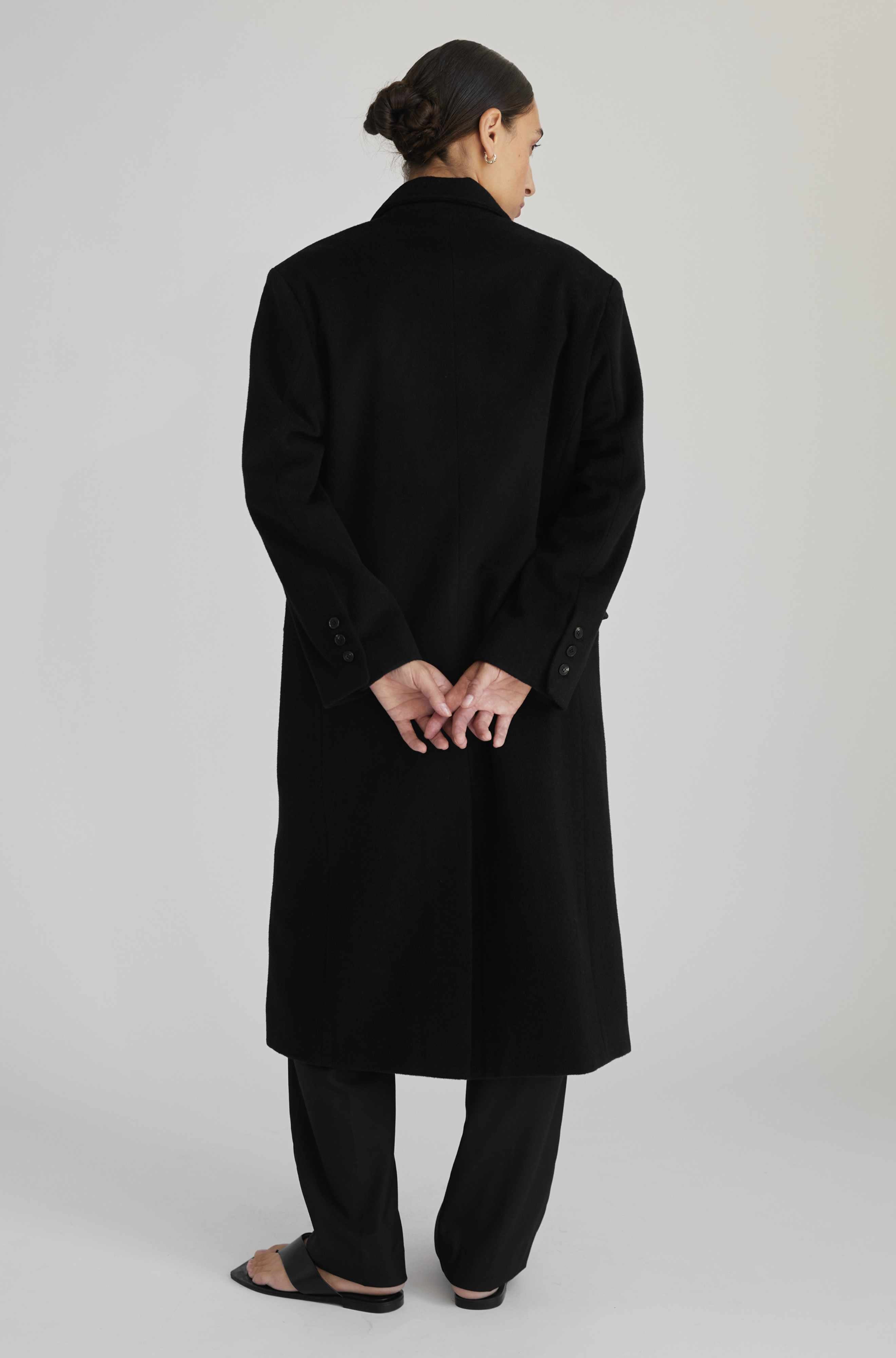Person wearing a black coat on a plain background