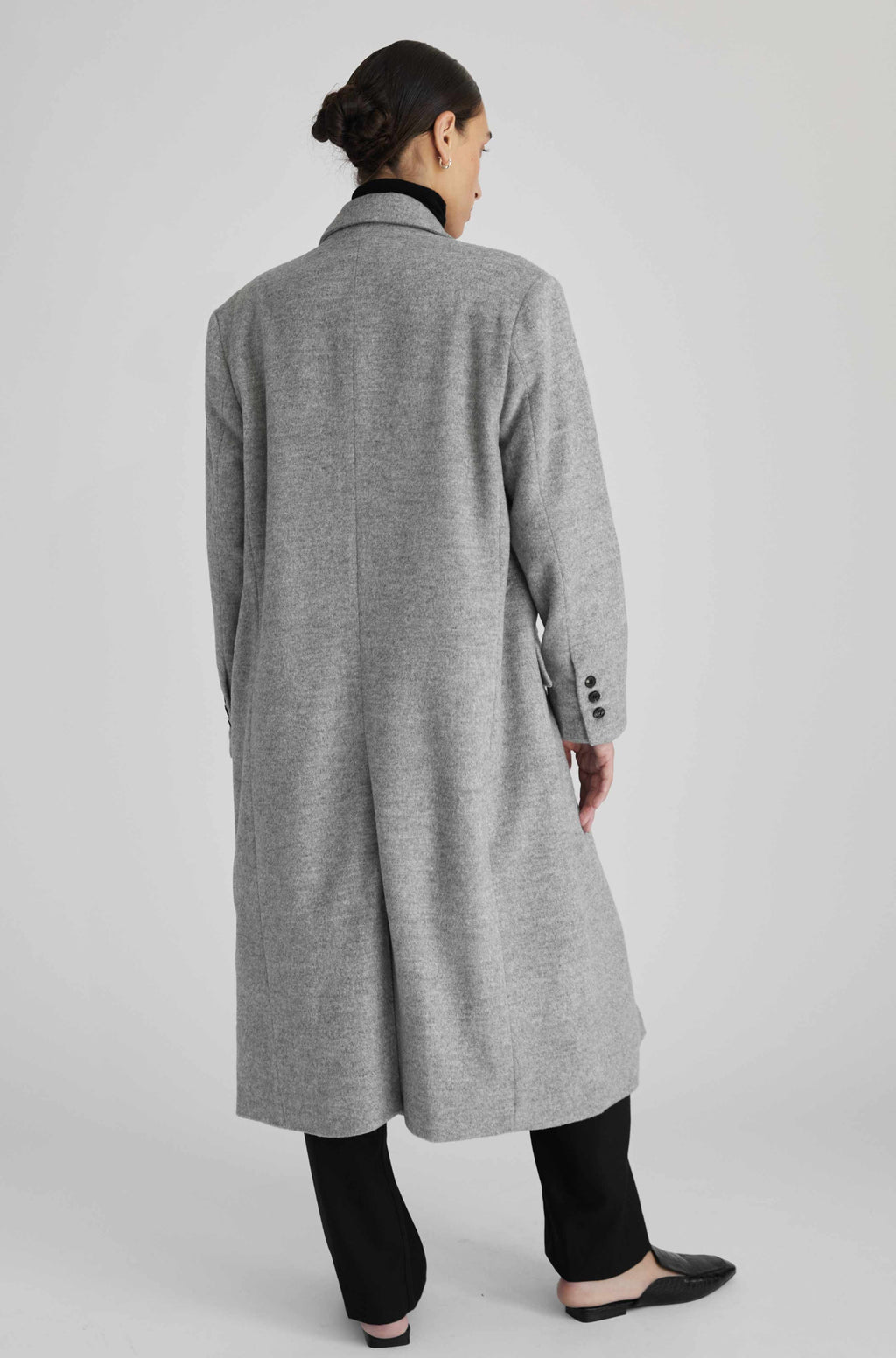 Person wearing a gray coat from behind on a light gray background