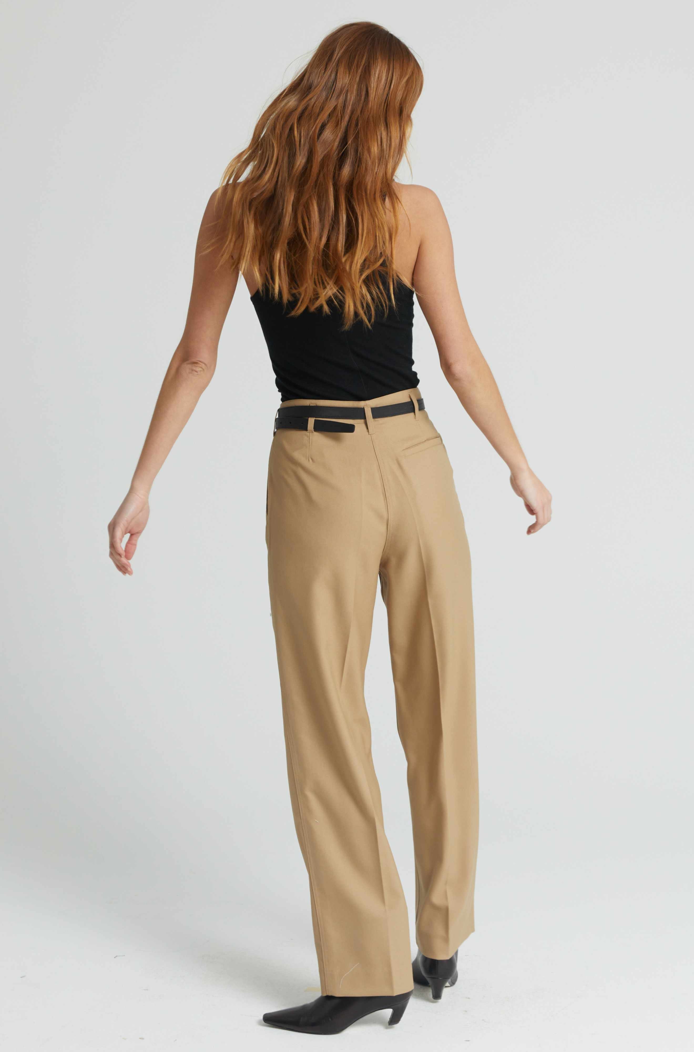 Woman wearing beige pants and a black top on a white background
