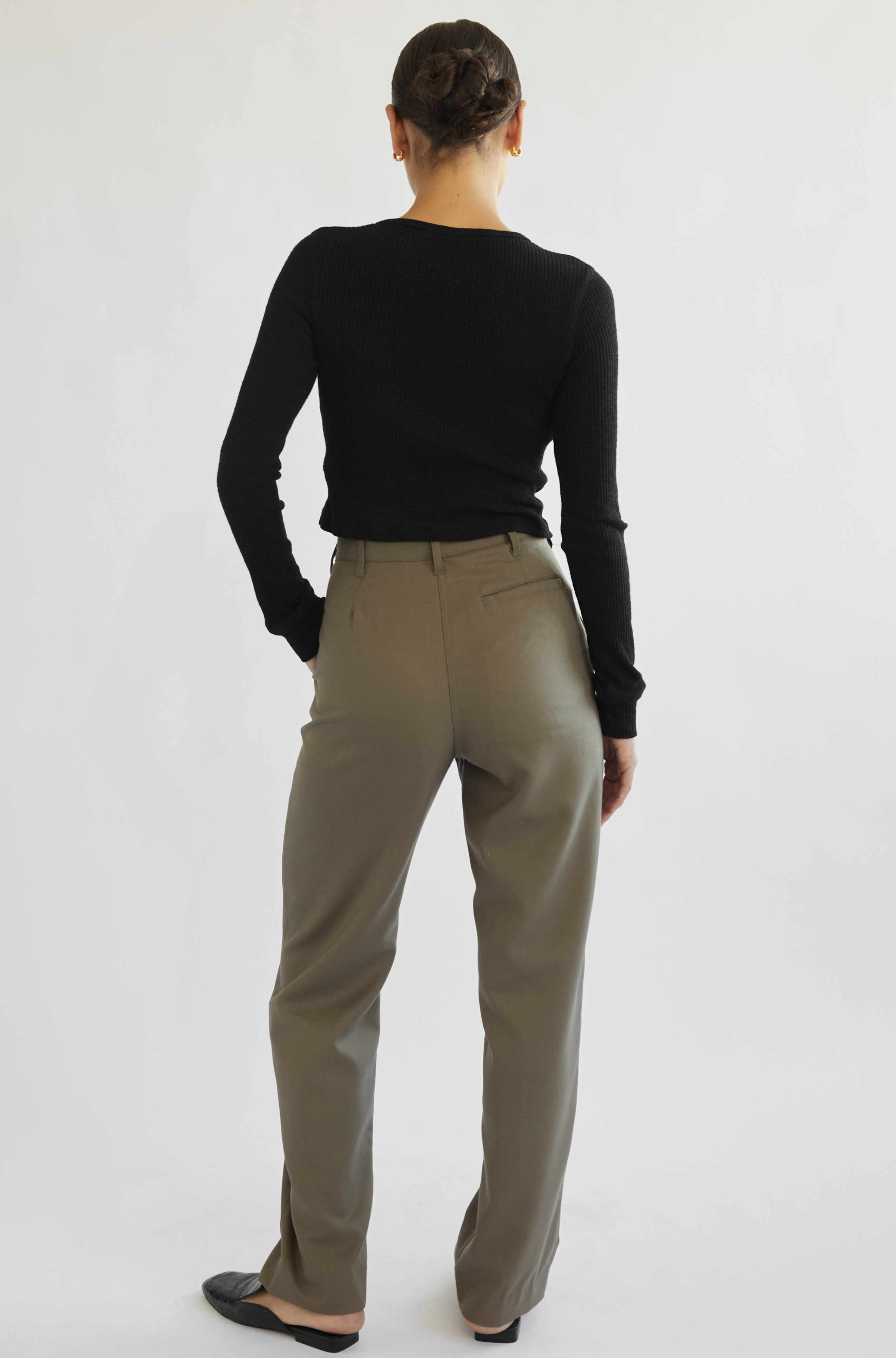 Person wearing a black long-sleeve top and beige pants on a white background