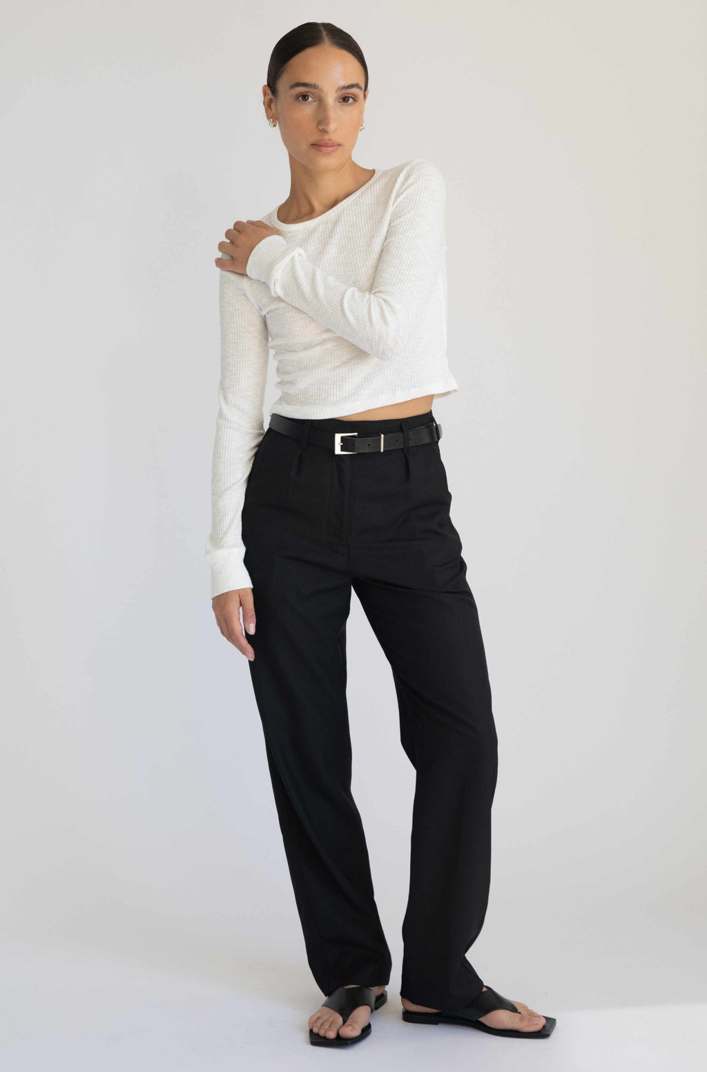 Woman wearing a white long-sleeve top and black pants against a white background