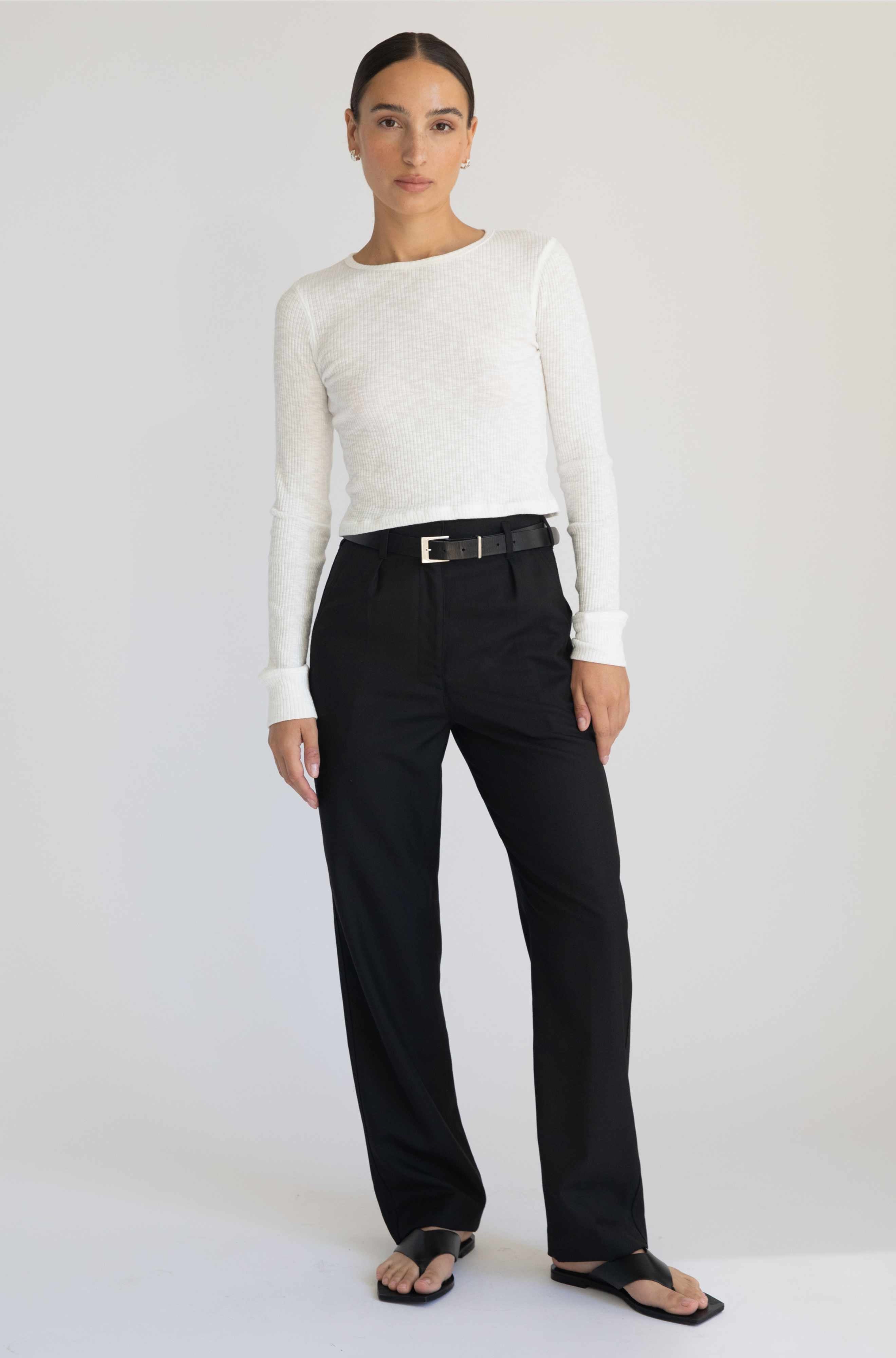 Woman wearing a white long-sleeve top and black pants on a white background