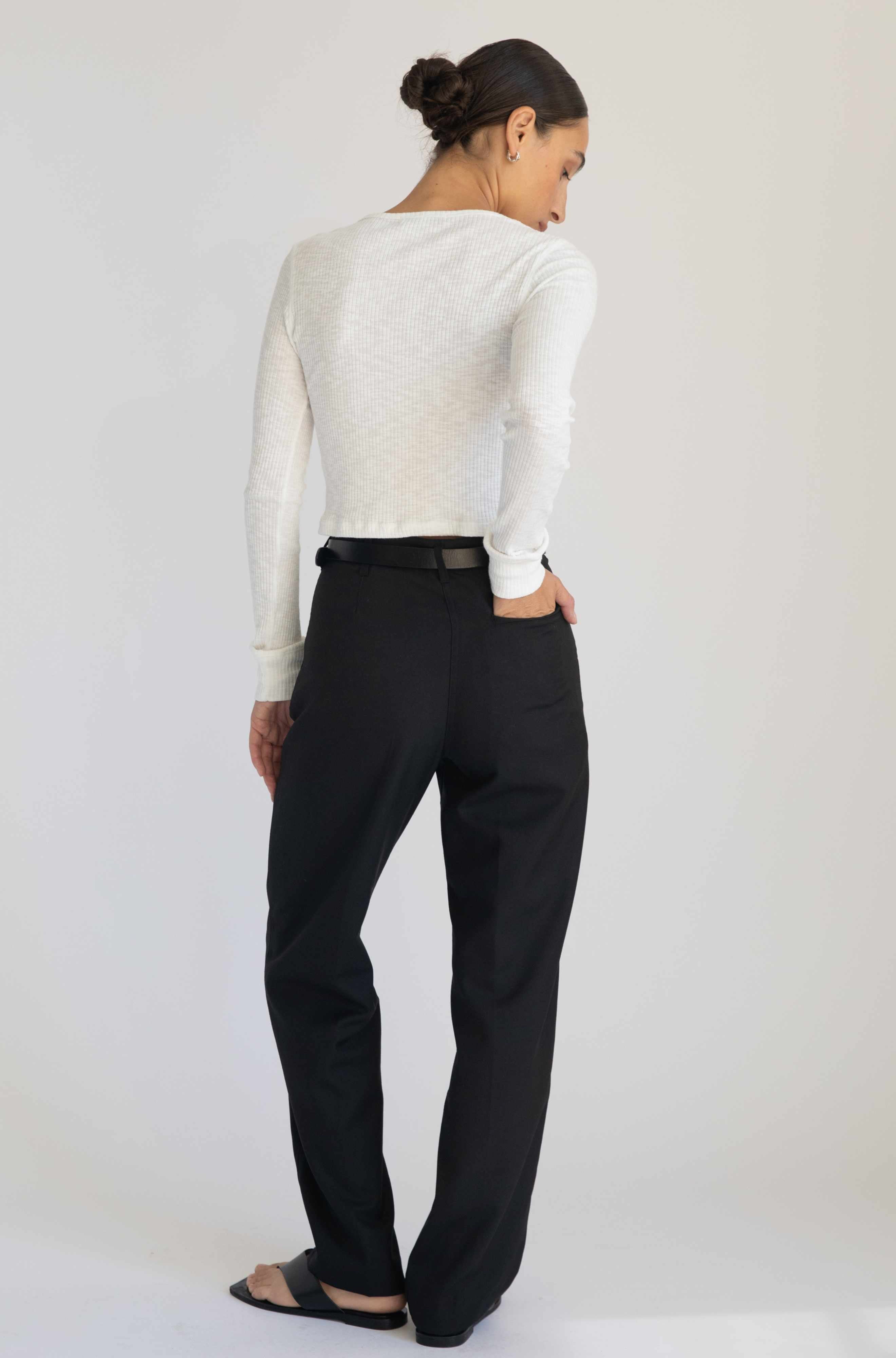 Person wearing a white sweater and black pants on a plain background
