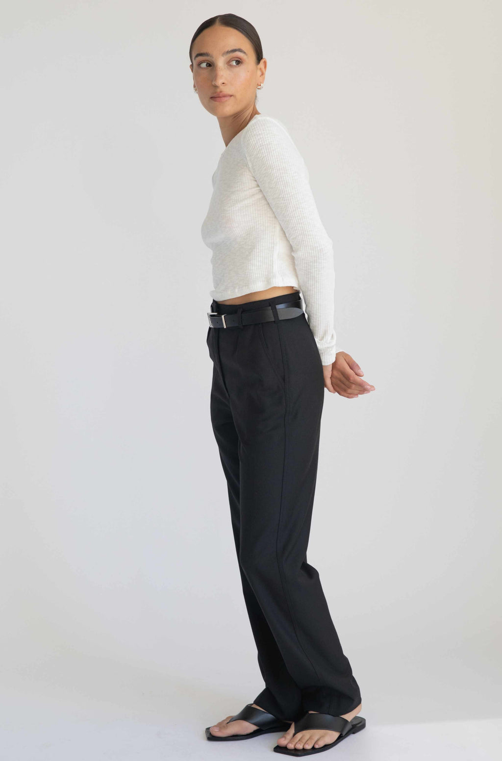 Woman wearing a white long-sleeve top and black pants against a white background