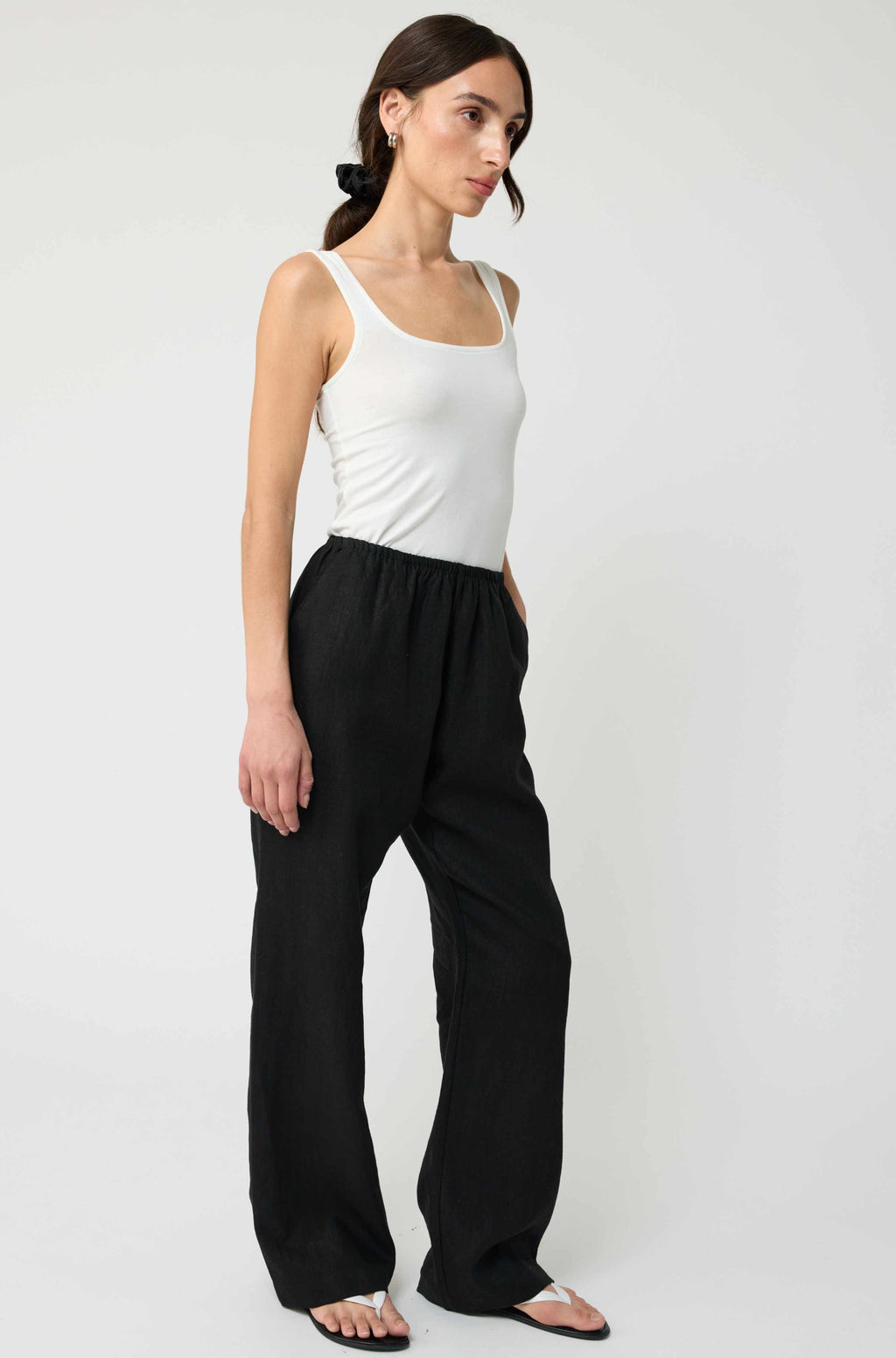 Woman wearing a white tank top and black pants on a white background