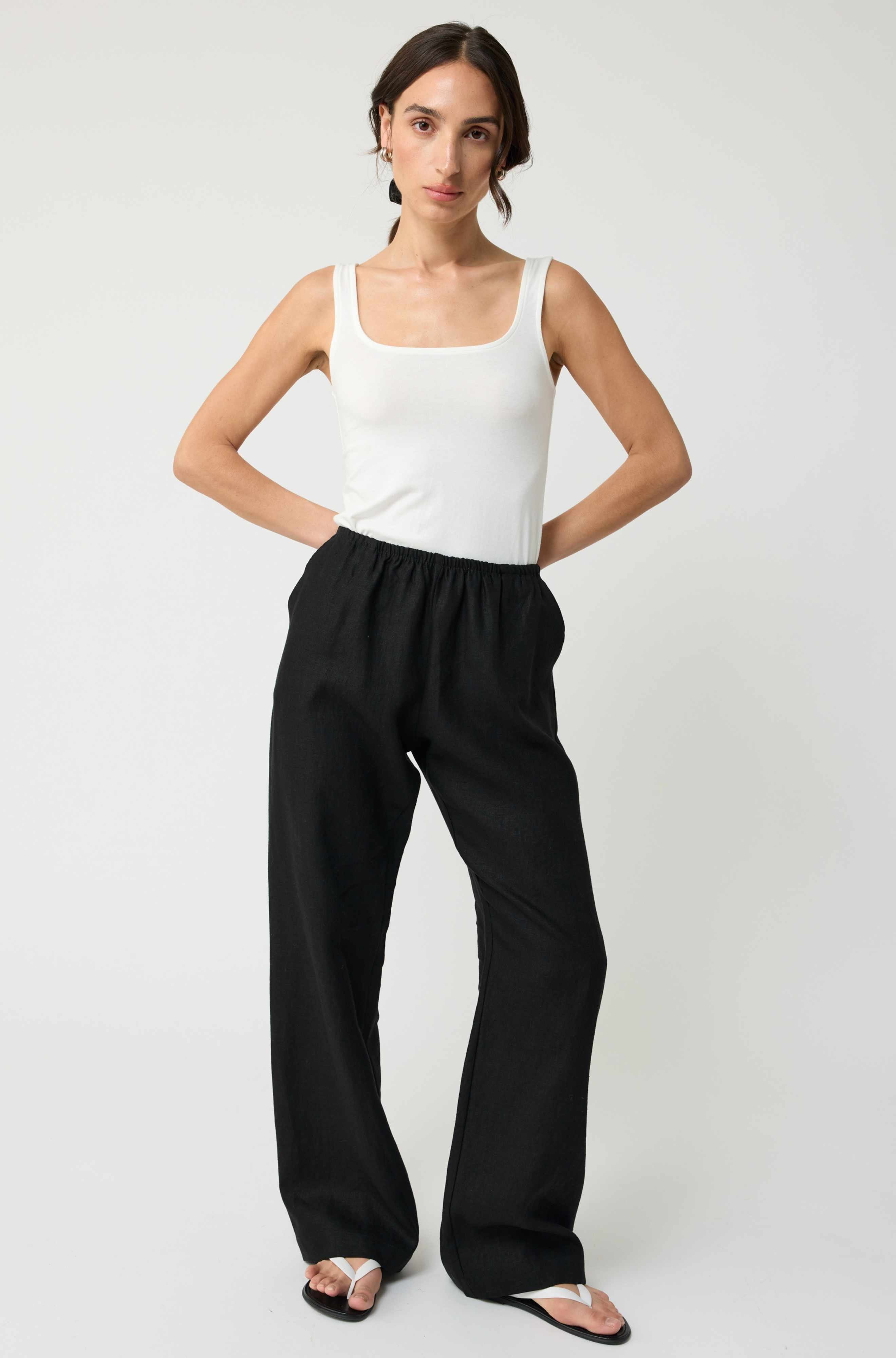 Woman wearing a white tank top and black pants on a white background