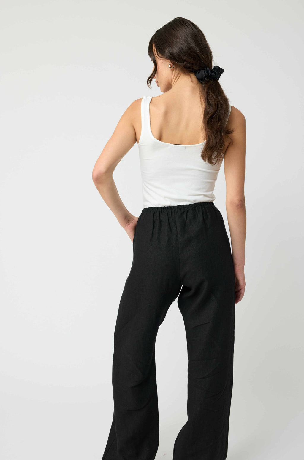 Woman wearing a white tank top and black pants on a plain background