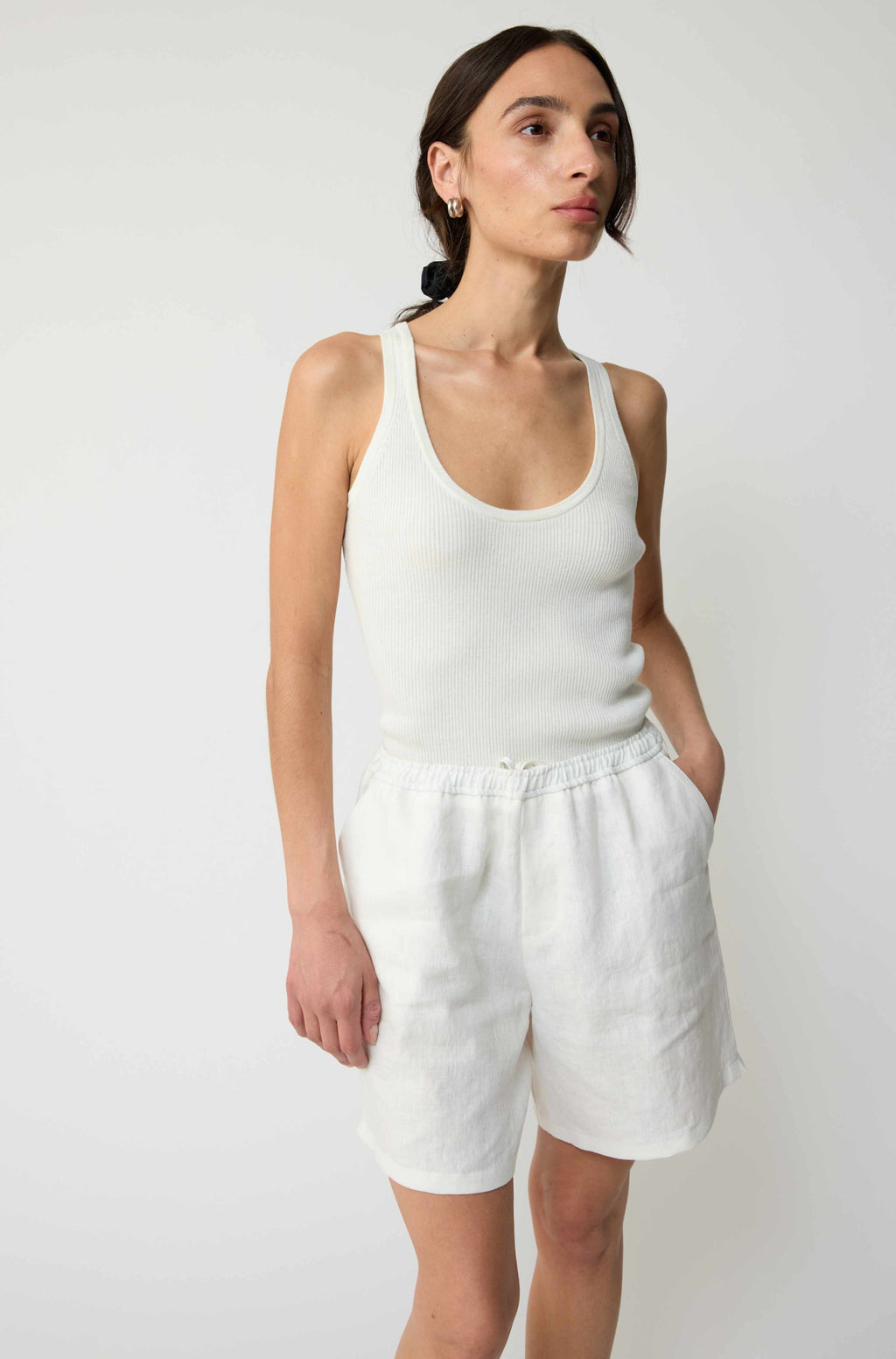 Woman wearing a white tank top and shorts against a plain background