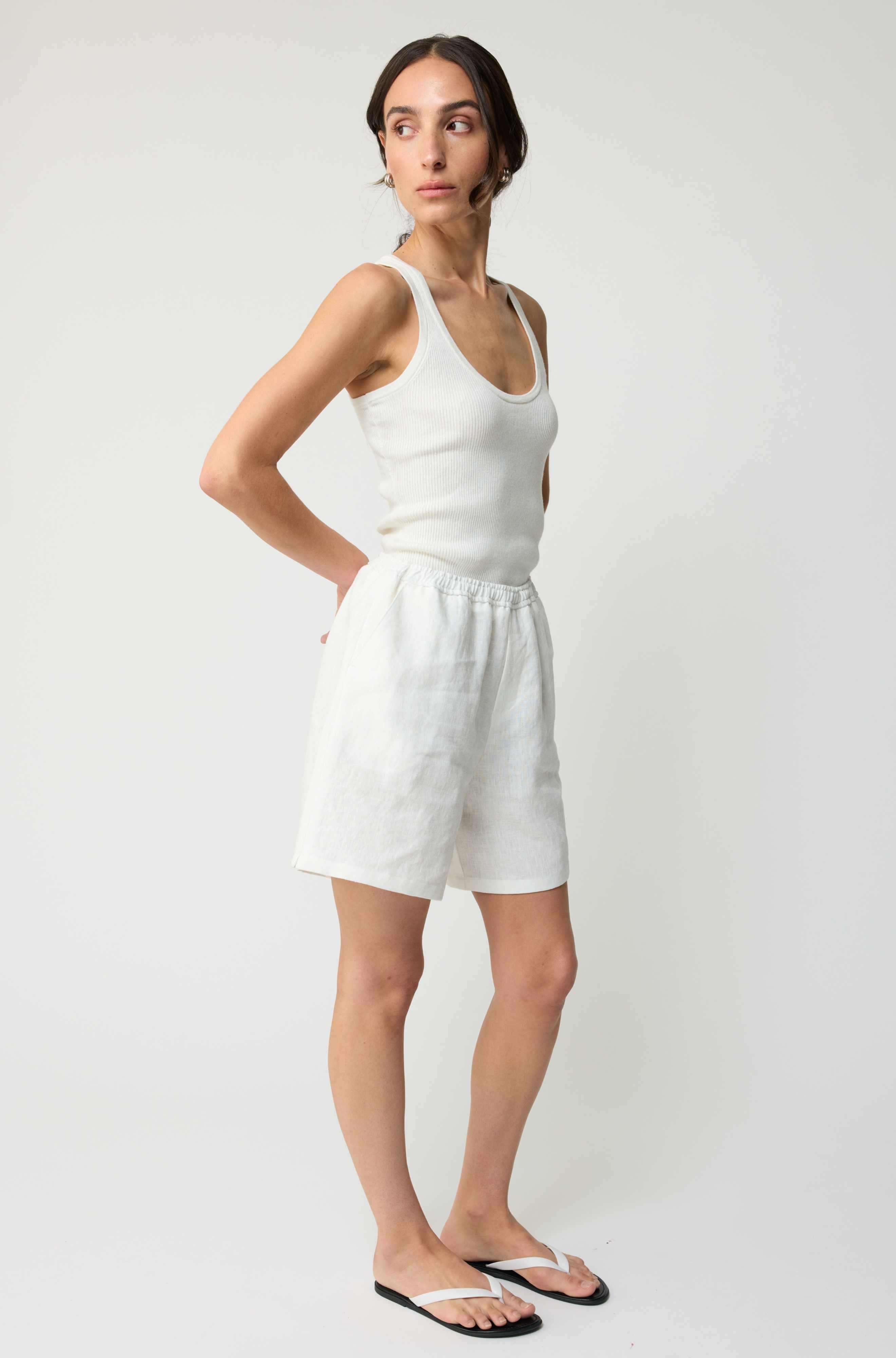 Woman wearing a white tank top and shorts on a plain background