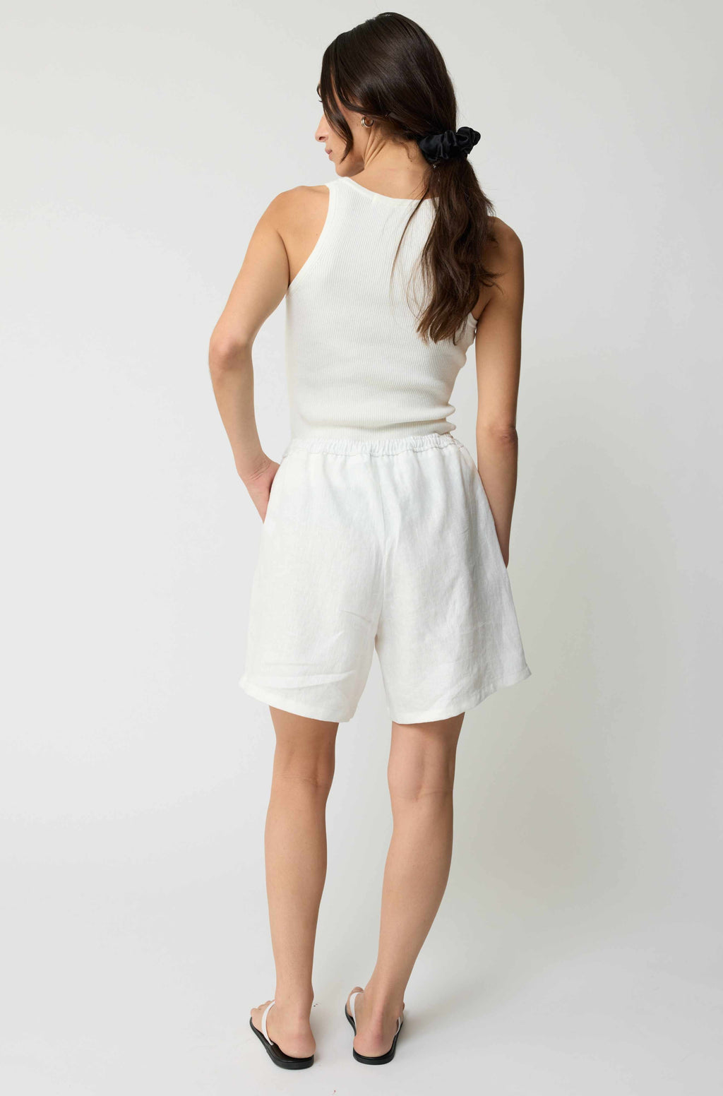 Woman wearing a white sleeveless top and shorts on a plain background