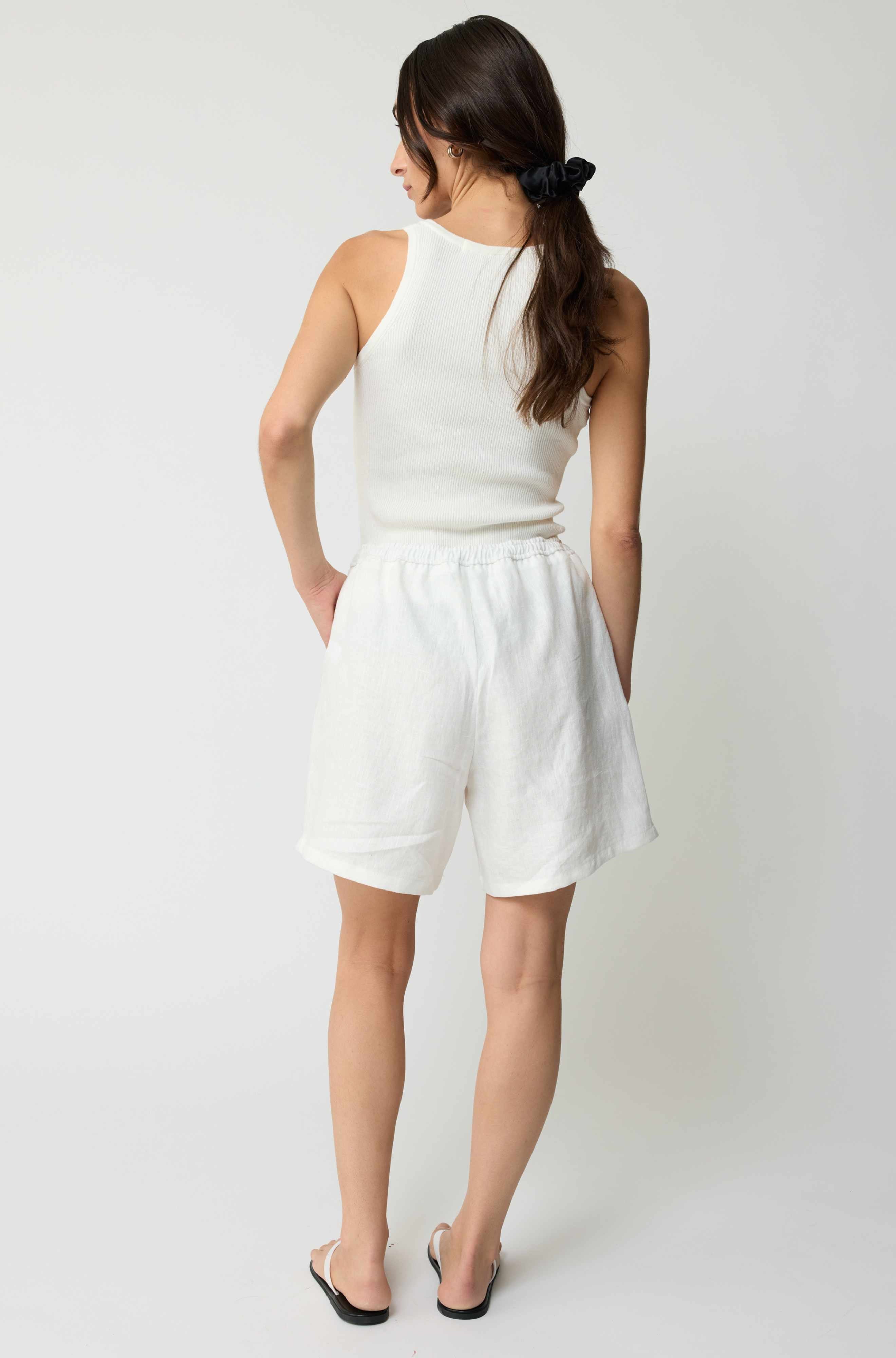 Woman wearing a white sleeveless top and shorts on a plain background