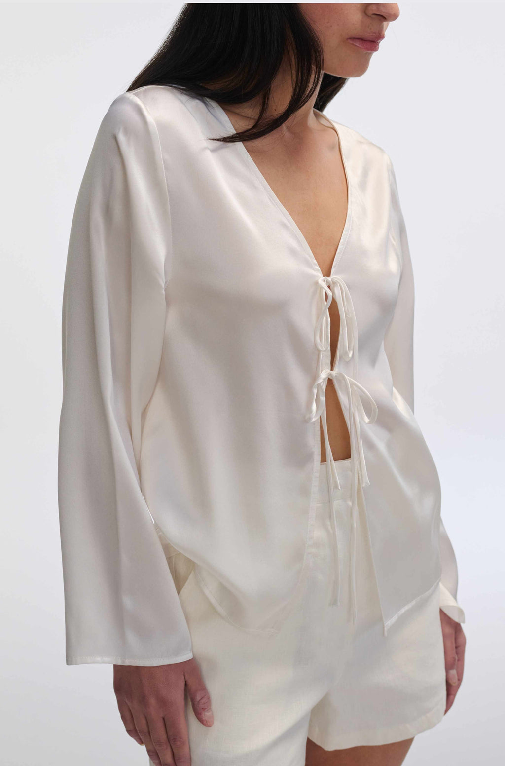 White satin outfit with long sleeves and shorts on a plain background