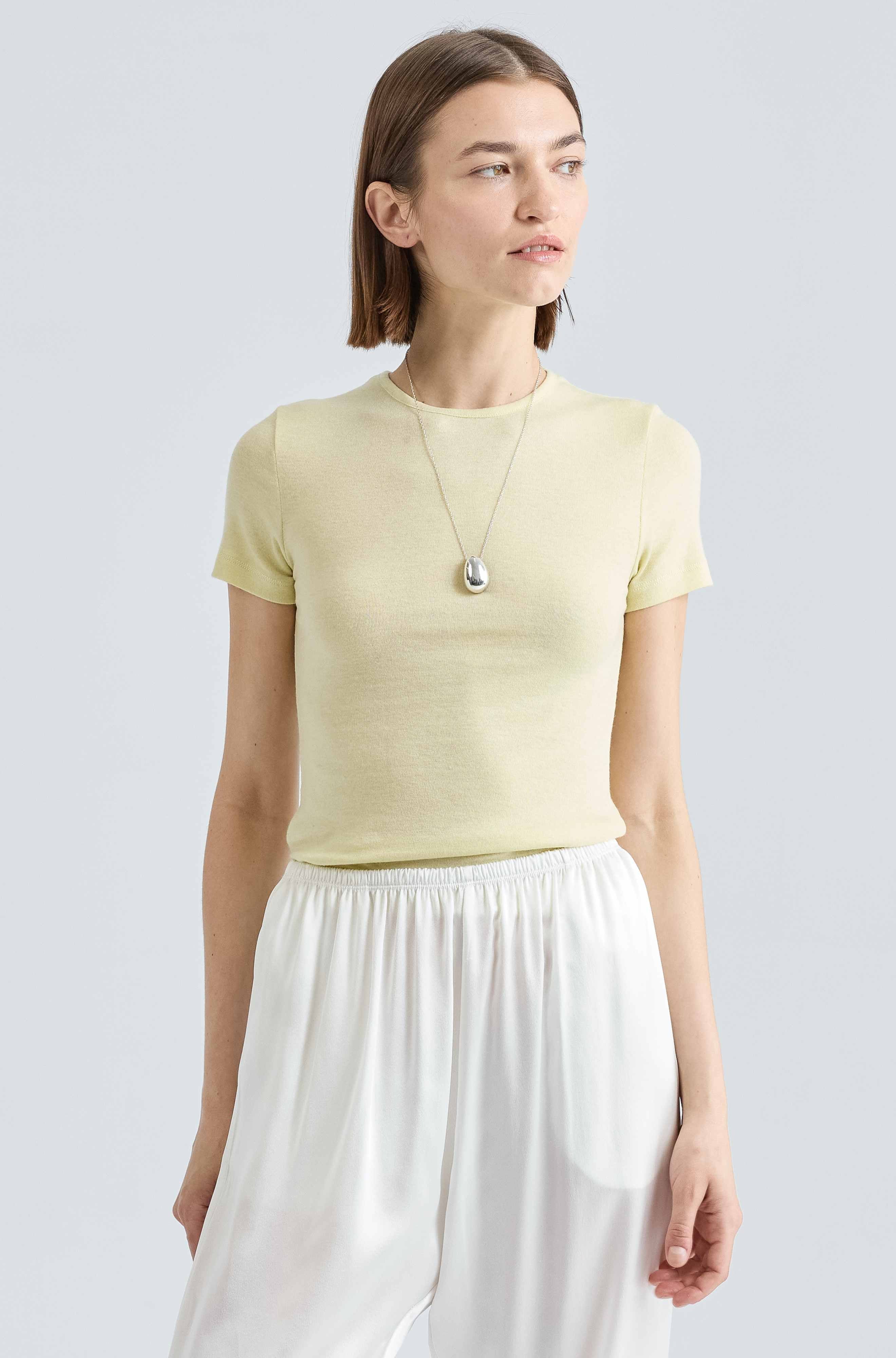 Woman wearing a yellow knit tee with a silver necklace and white silk pants