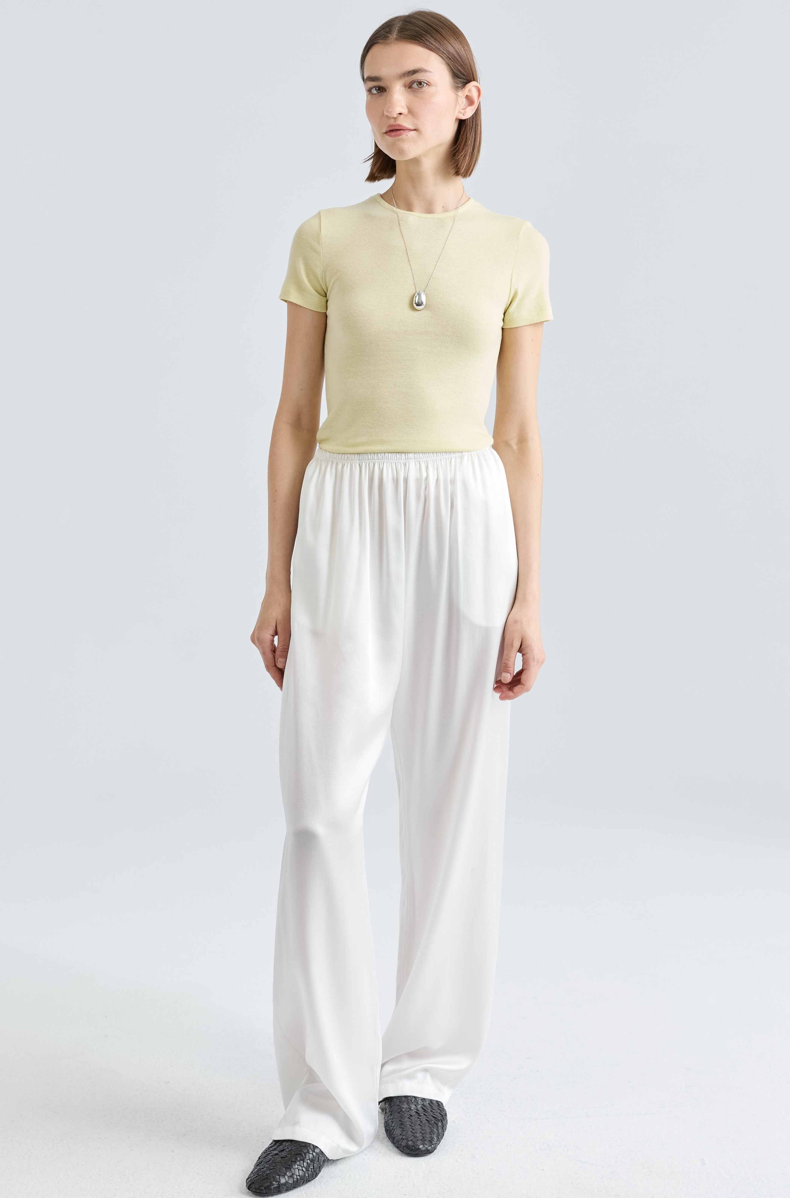 Woman wearing a light yellow top and white pants on a plain background