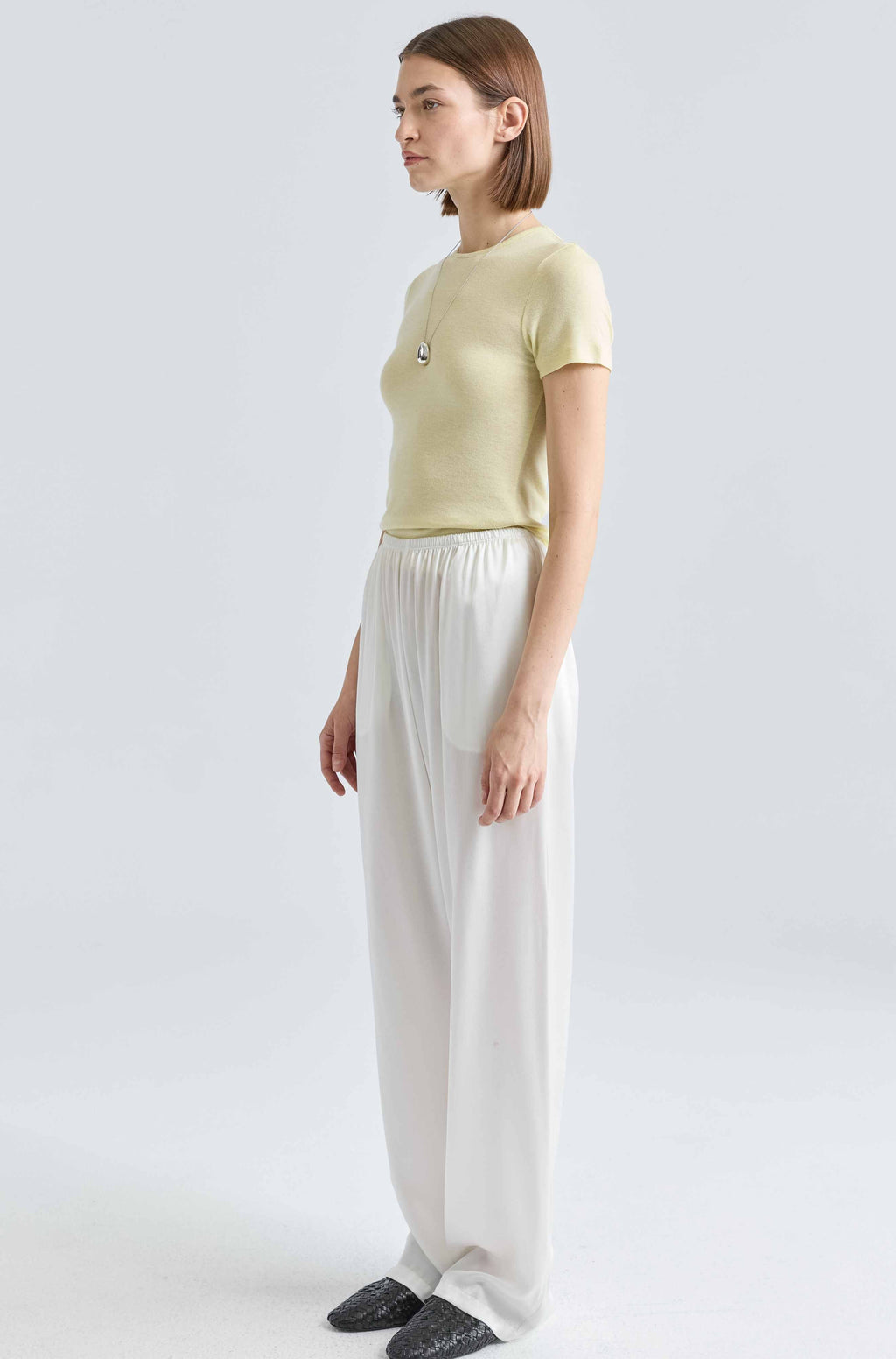Woman wearing a yellow knit tee with a silver necklace and white silk pants