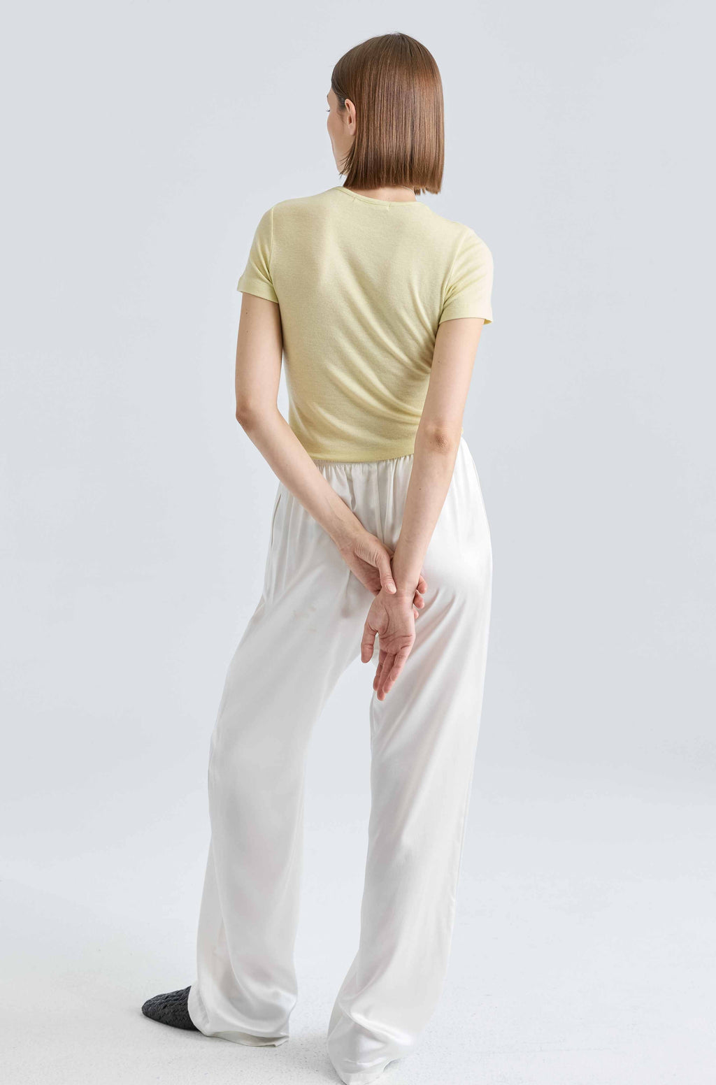 Person wearing a yellow top and white pants on a light gray background