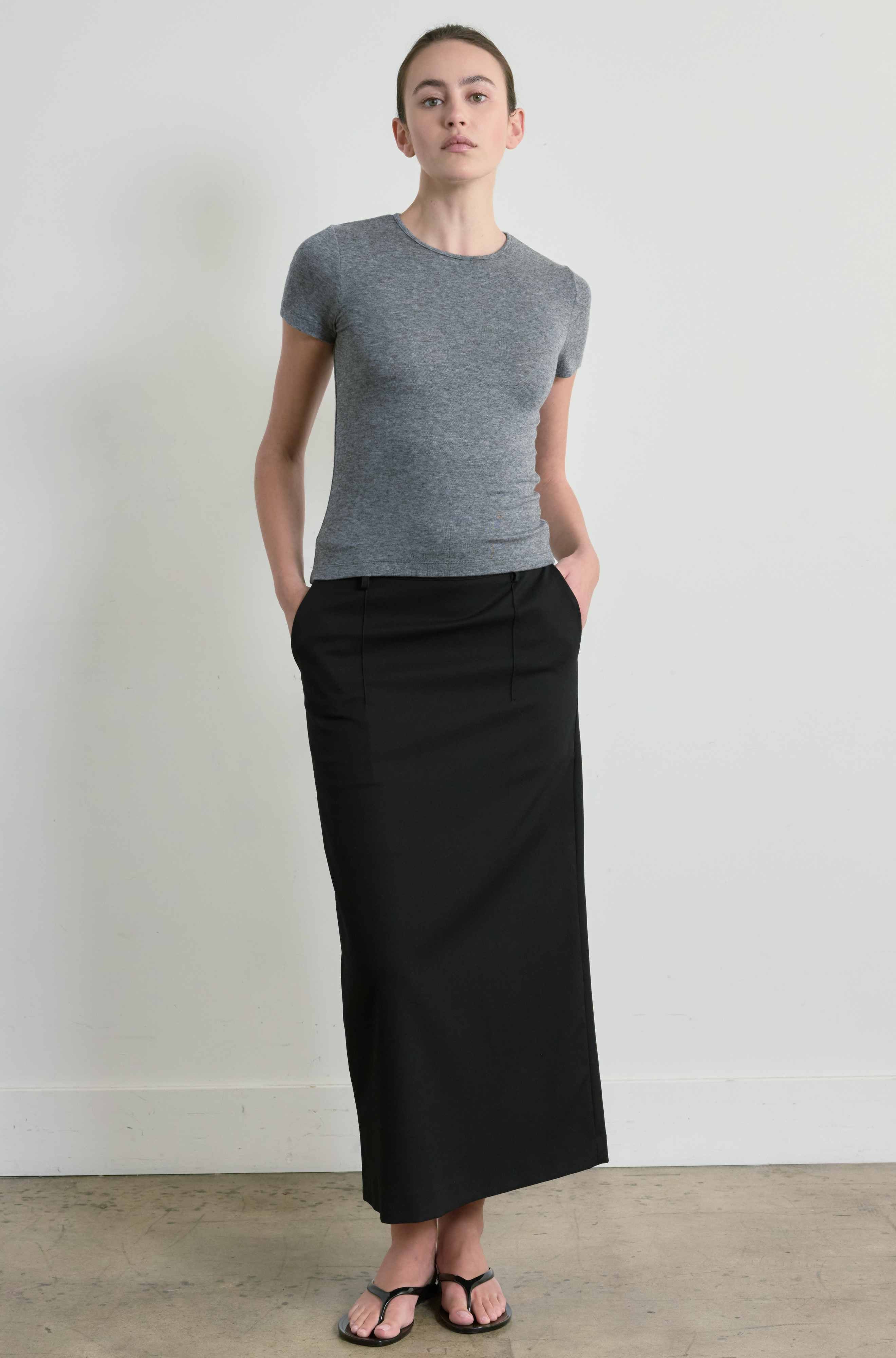 Person wearing a gray short-sleeve top and black long skirt against a white background