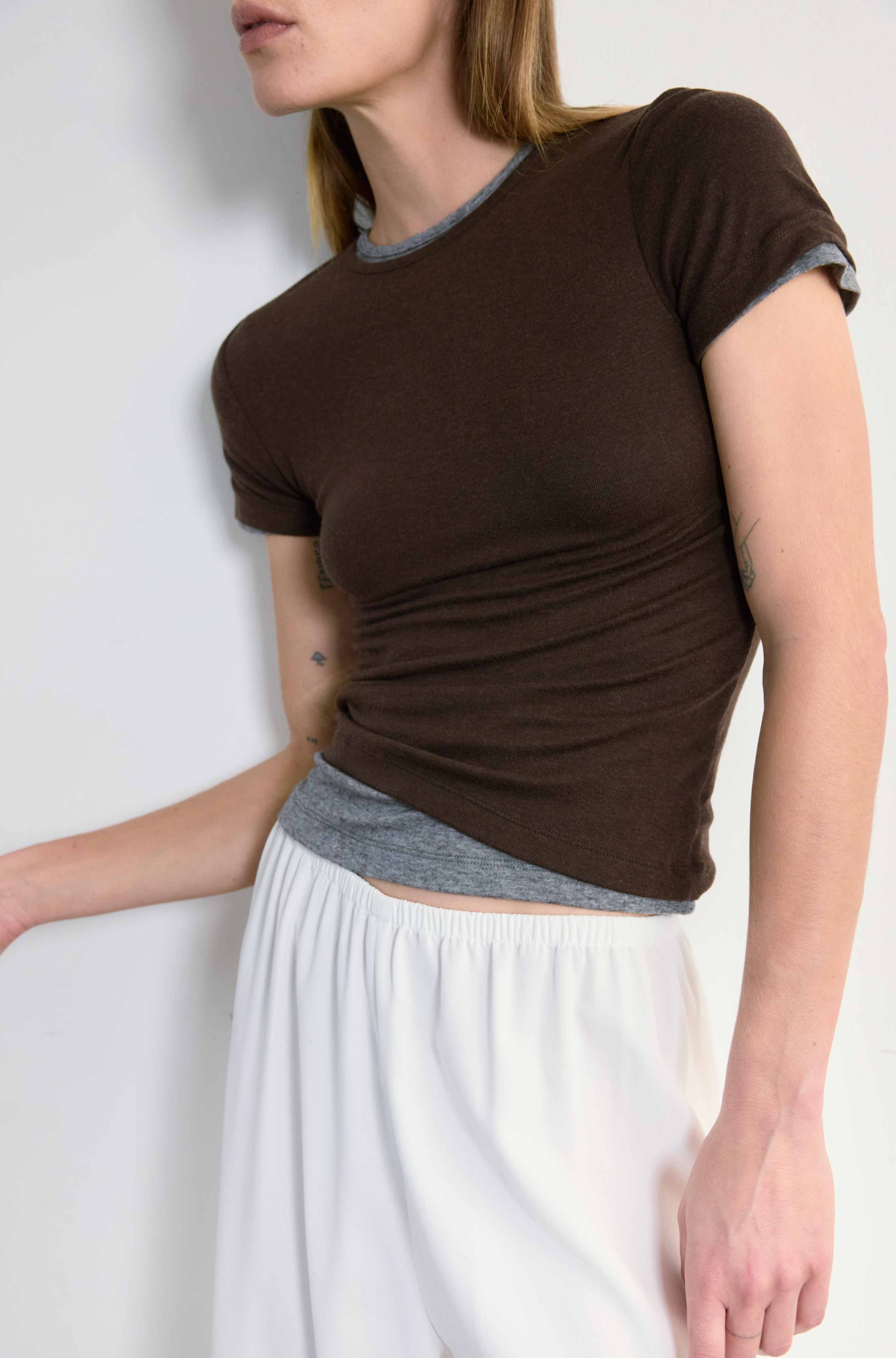 Woman wearing a brown top with a gray trim and white pants against a plain background