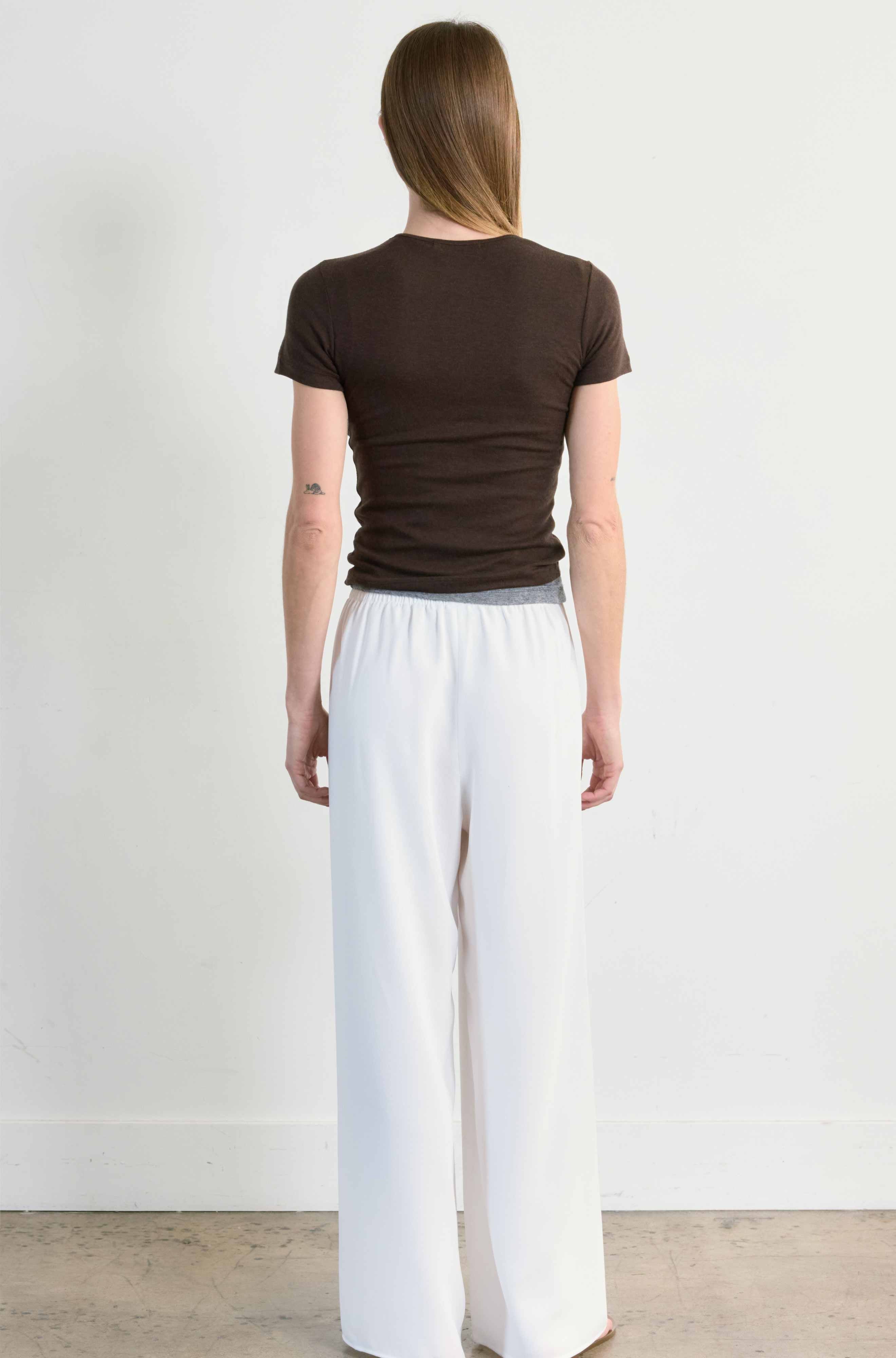 Person wearing a brown t-shirt and white pants standing against a plain background