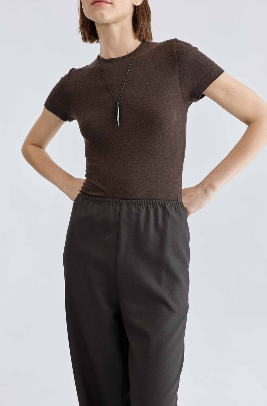 Person wearing a brown top and black pants on a light gray background