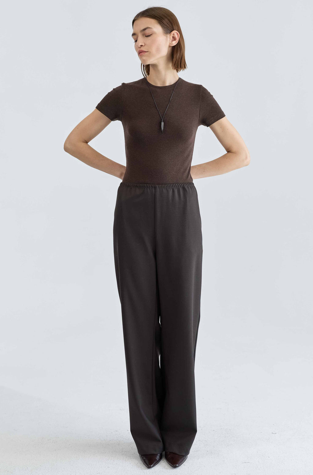 Woman wearing a brown top and black pants on a light gray background