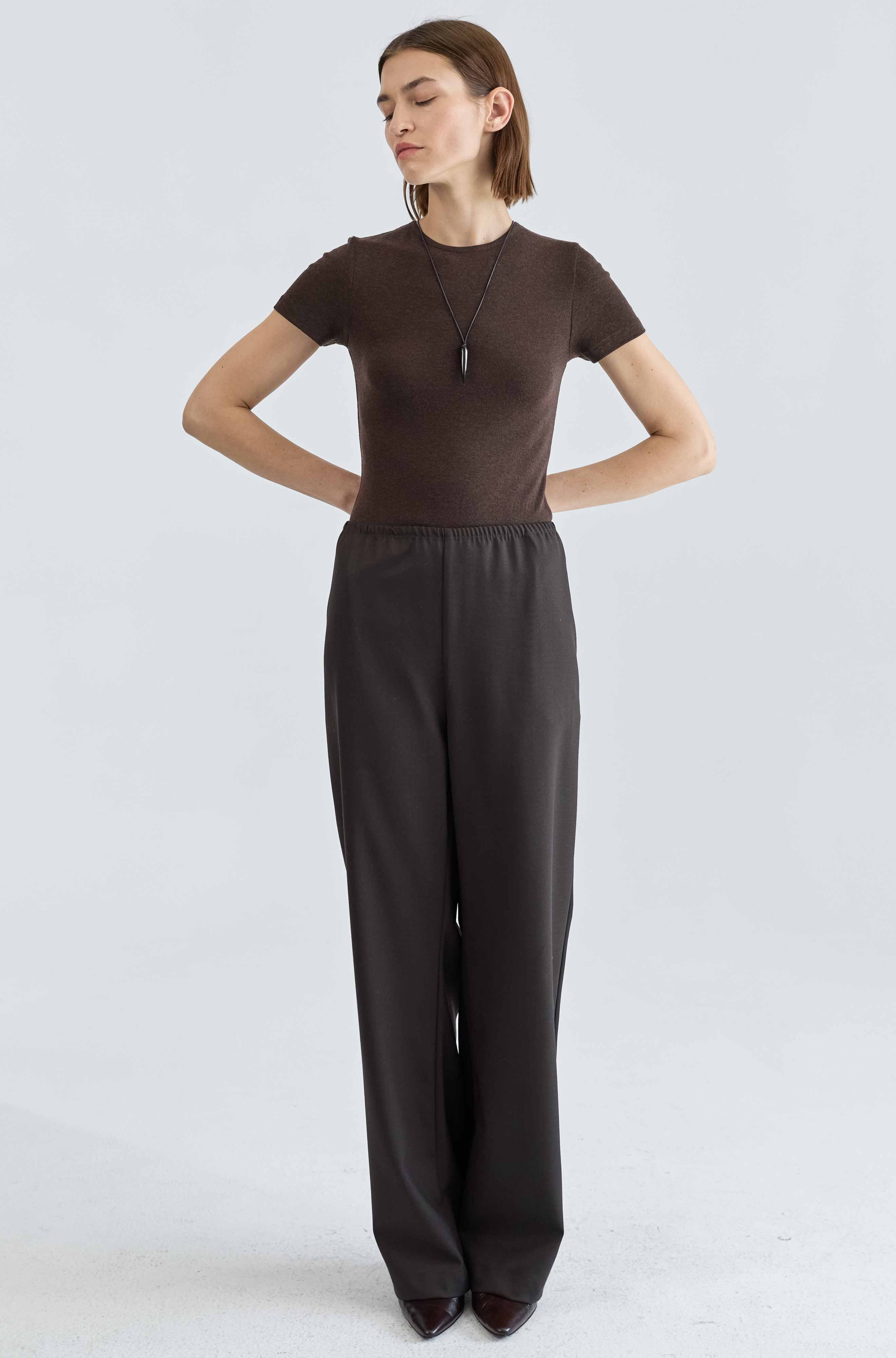 Woman wearing a brown top and black pants on a light gray background